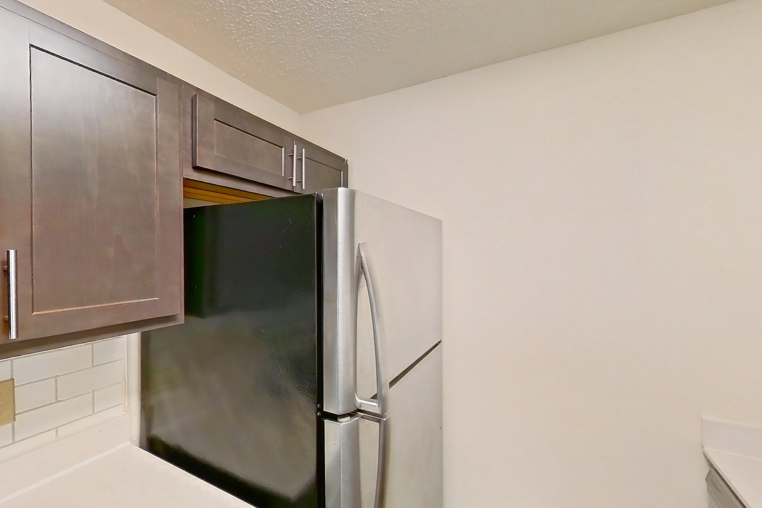 Kitchen with dark wood-finish flooring, electric range, light countertops, light stone countertops, light wood-finish flooring, microwave, oven/range, refrigerator, and stainless steel appliances, Apartment 2225-B at The Landings