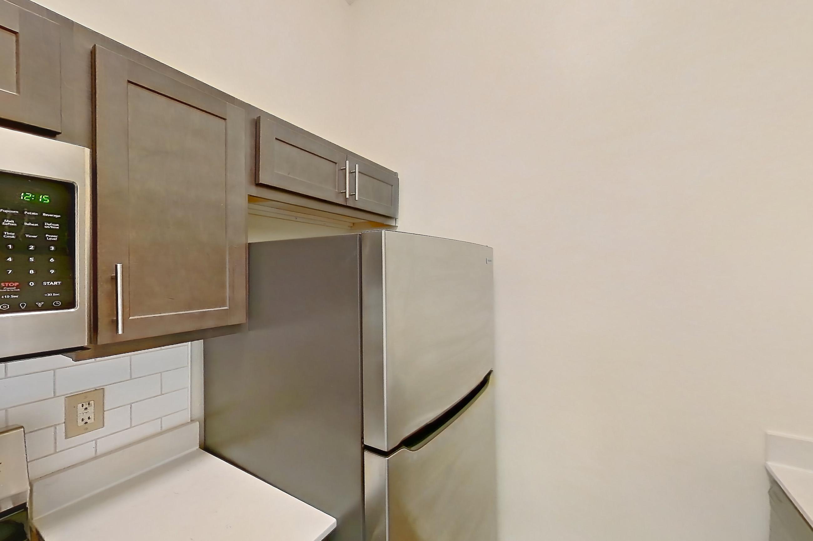 Kitchen with electric range, light countertops, light stone countertops, light wood-finish flooring, microwave, oven/range, refrigerator, and stainless steel appliances, Apartment 2209-L at The Landings