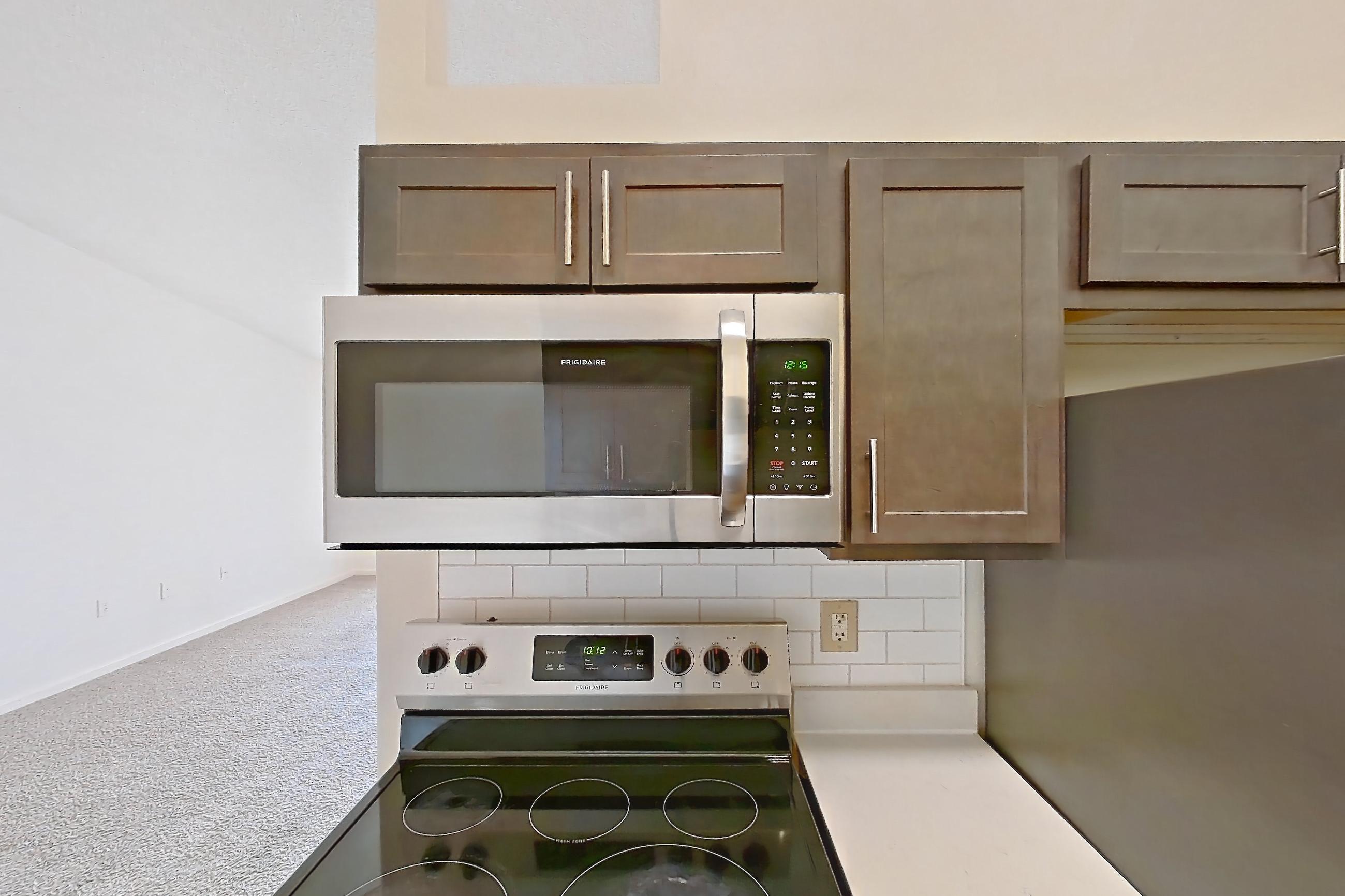 Kitchen with electric range, light countertops, light stone countertops, light wood-finish flooring, microwave, oven/range, refrigerator, and stainless steel appliances, Apartment 2209-L at The Landings