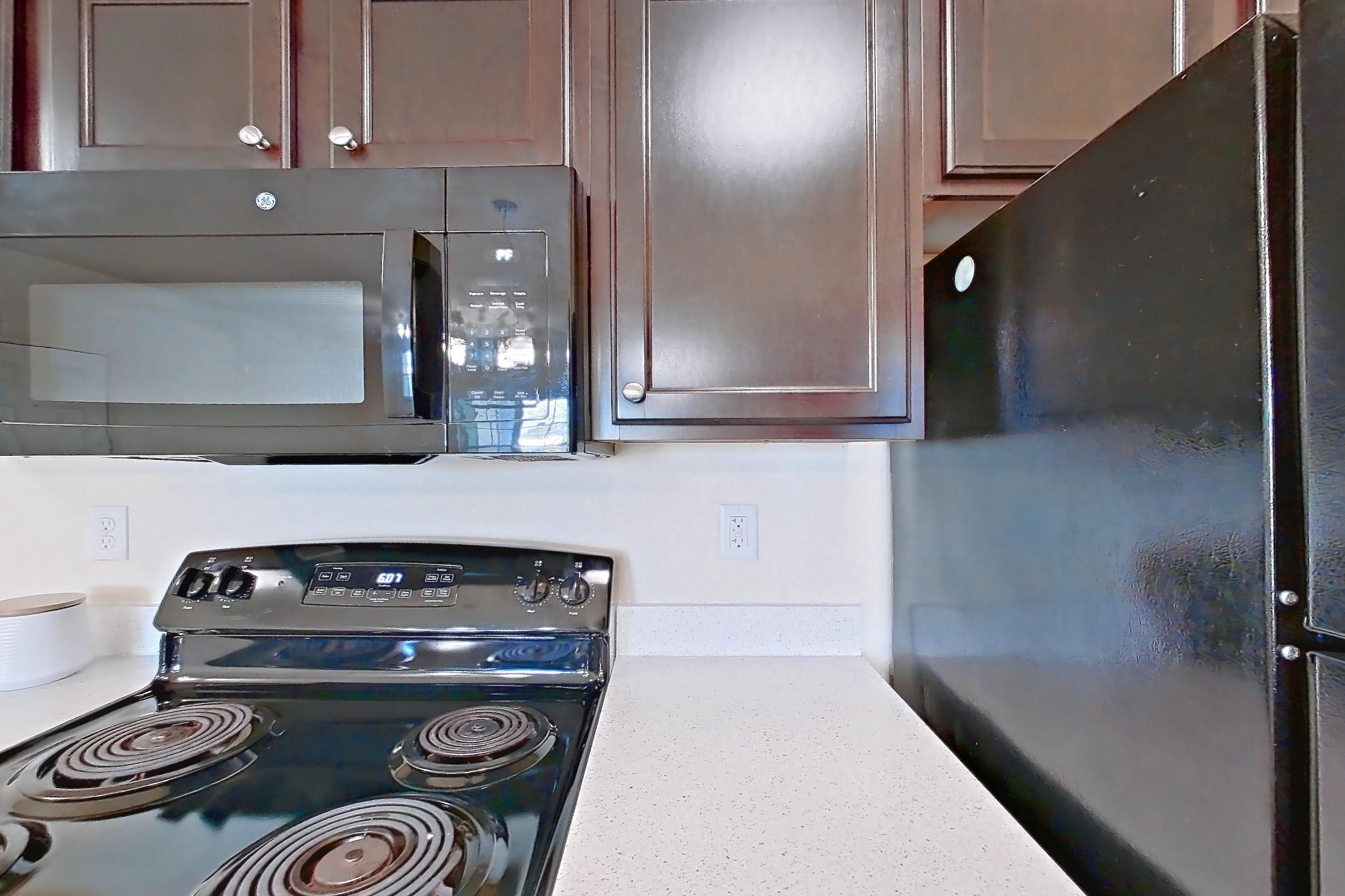 Kitchen with black appliances, dark carpet, dark wood-finish flooring, dishwasher, electric range, light countertops, light stone countertops, microwave, oven/range, and refrigerator, Apartment 1232 at William Cannon