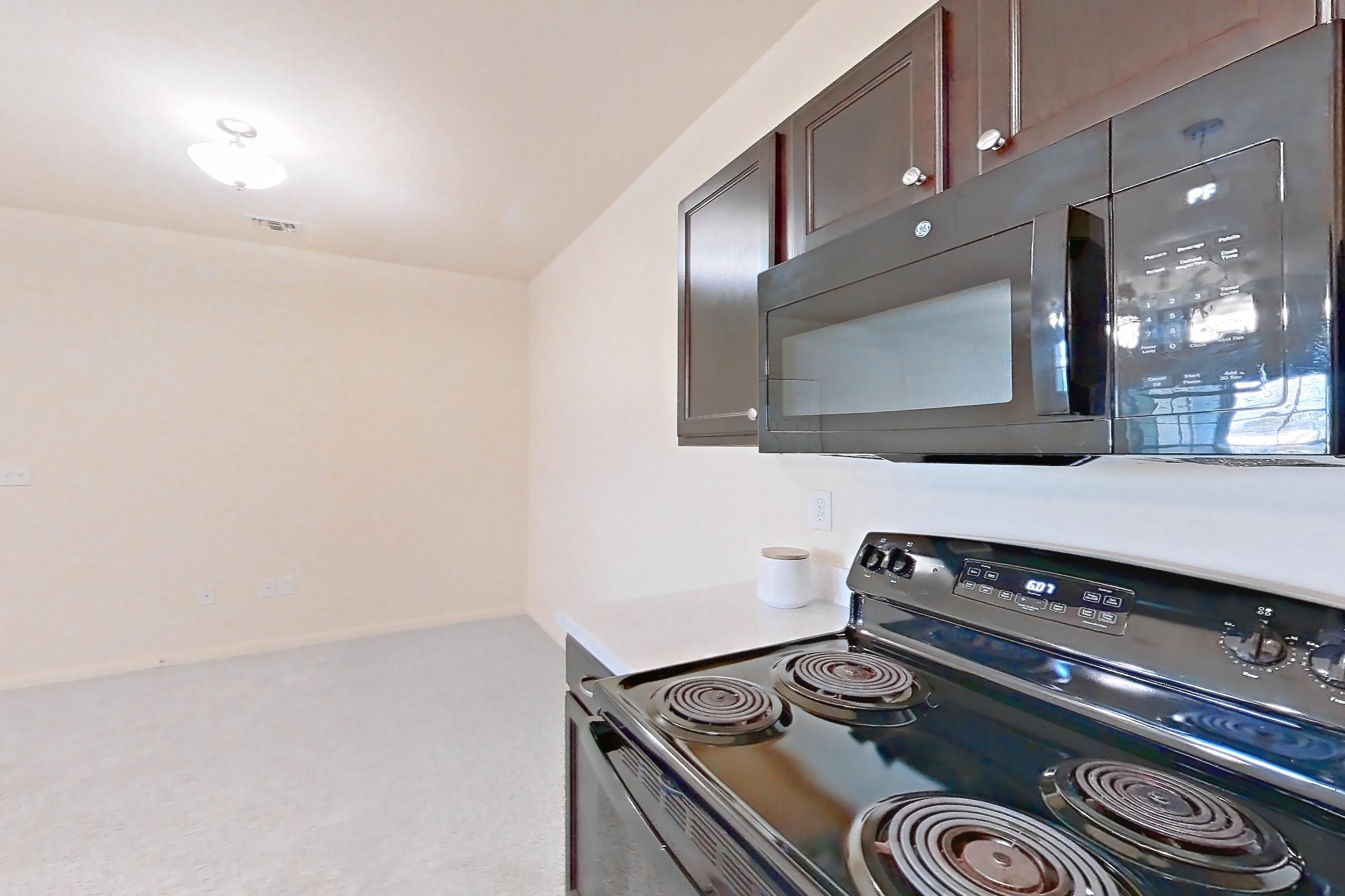 Kitchen with black appliances, dark carpet, dark wood-finish flooring, dishwasher, electric range, light countertops, light stone countertops, microwave, oven/range, and refrigerator, Apartment 1232 at William Cannon