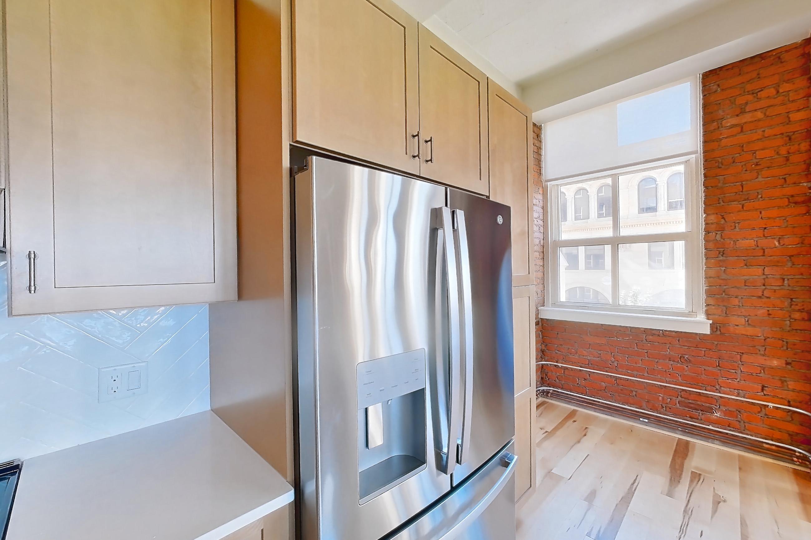 Kitchen with electric range, light countertops, light wood-finish flooring, oven/range, range hood, refrigerator, stainless steel appliances, and water & ice dispenser, Unit 310 at Temple Building