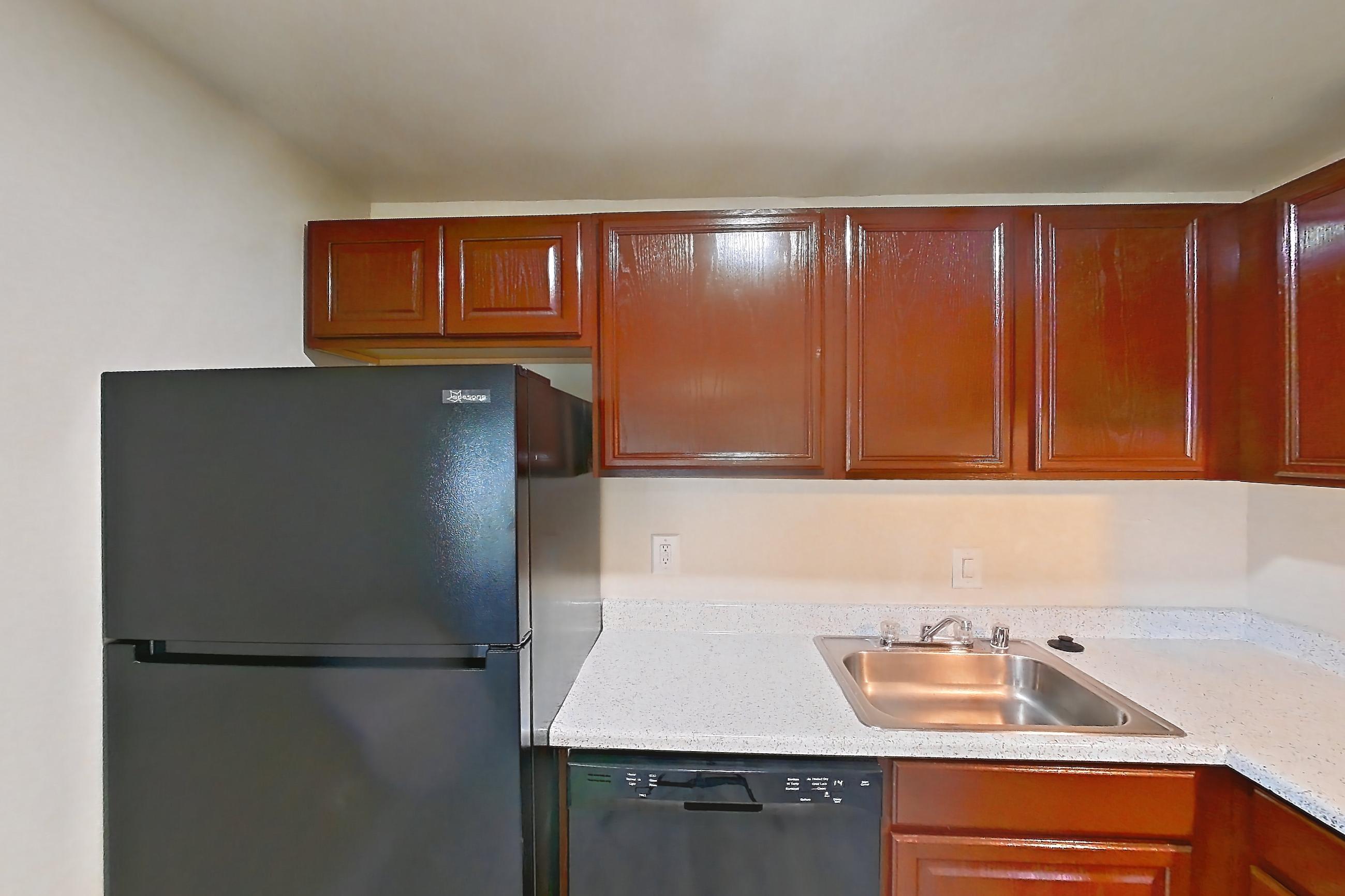 Kitchen with black appliances, dishwasher, gas range, light countertops, light stone countertops, light wood-finish flooring, oven/range, range hood, and refrigerator, Apartment 9112ER12 at Franklin Park at Greenbelt Station