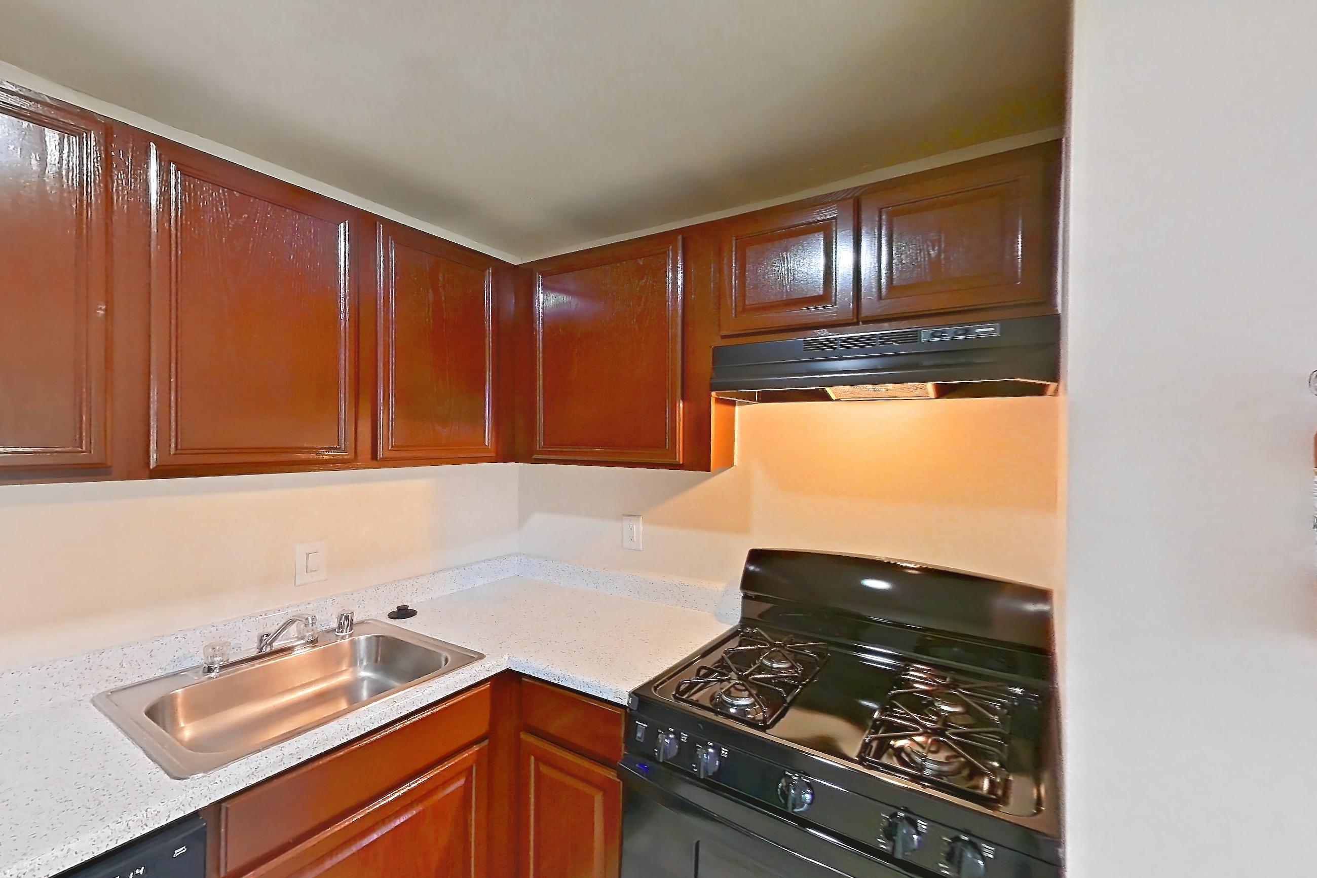 Kitchen with black appliances, dishwasher, gas range, light countertops, light stone countertops, light wood-finish flooring, oven/range, range hood, and refrigerator, Apartment 9112ER12 at Franklin Park at Greenbelt Station