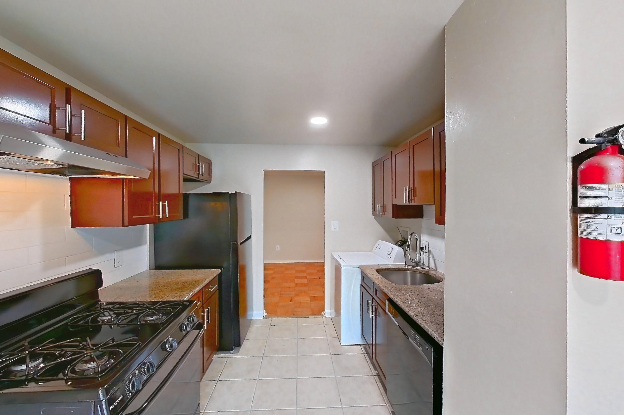 Kitchen with black appliances, dishwasher, gas range, in-unit laundry, light countertops, light stone countertops, light tile flooring, oven/range, refrigerator, and stainless steel appliances, Apartment 9320ER24 at Franklin Park at Greenbelt Station