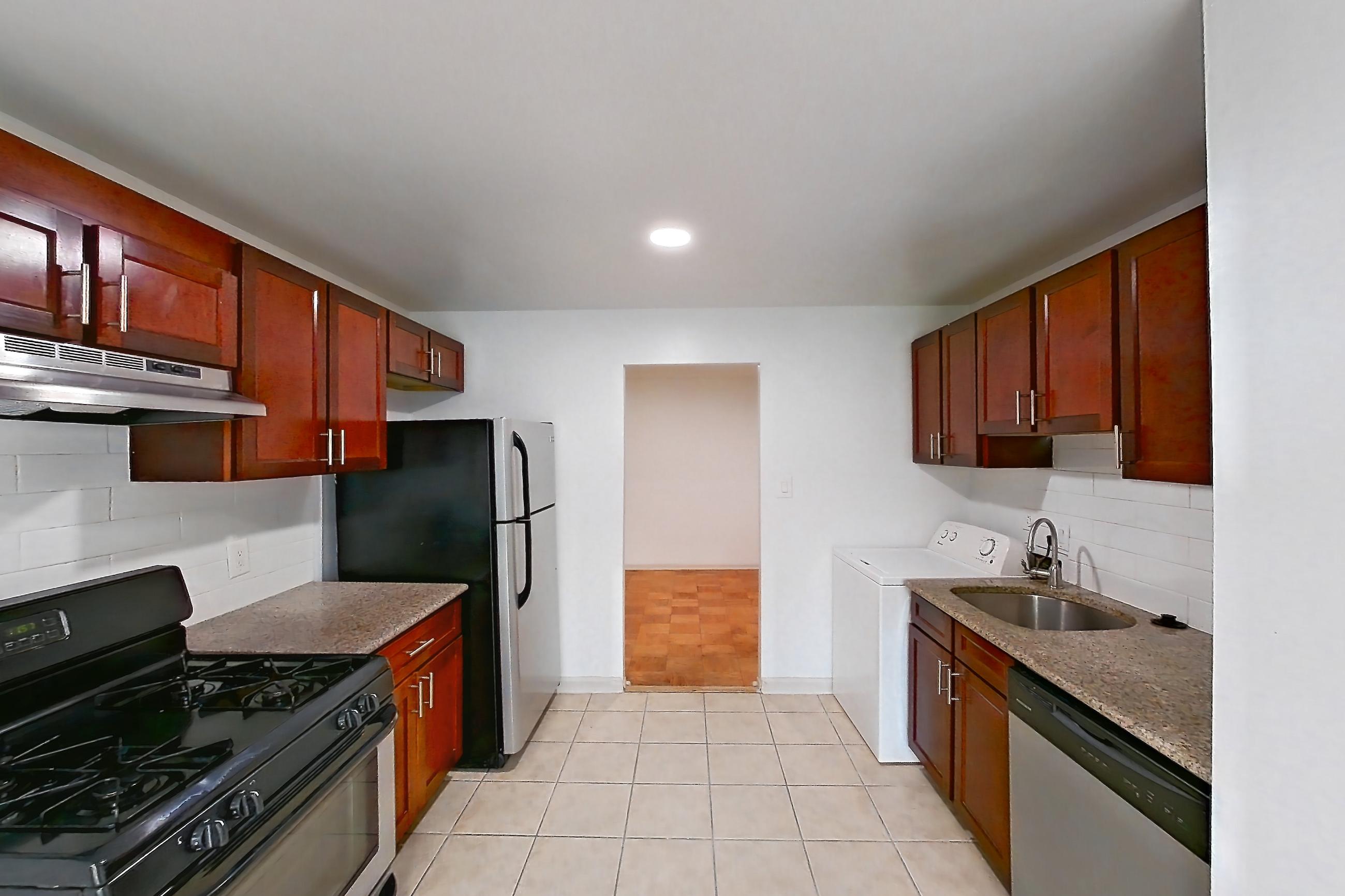 Kitchen with black appliances, dark stone countertops, dishwasher, gas range, in-unit laundry, light countertops, light tile flooring, oven/range, range hood, refrigerator, and stainless steel appliances, Apartment 9320ER22 at Franklin Park at Greenbelt Station