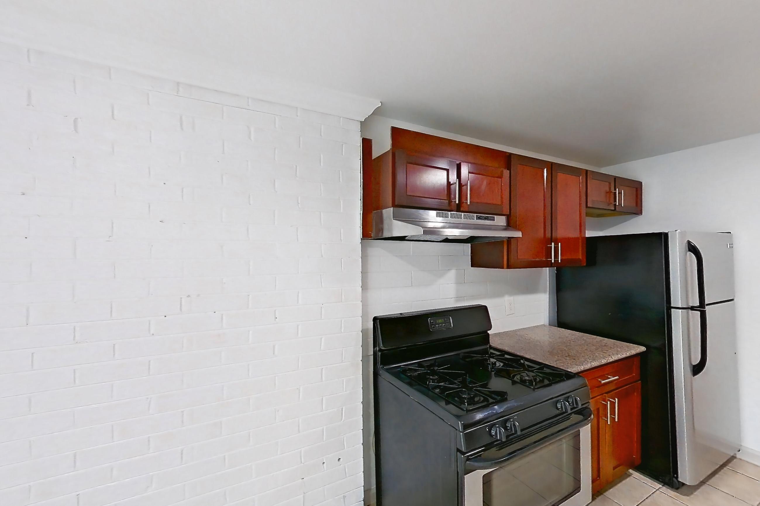 Kitchen with black appliances, dark stone countertops, dishwasher, gas range, in-unit laundry, light countertops, light tile flooring, oven/range, range hood, refrigerator, and stainless steel appliances, Apartment 9320ER22 at Franklin Park at Greenbelt Station