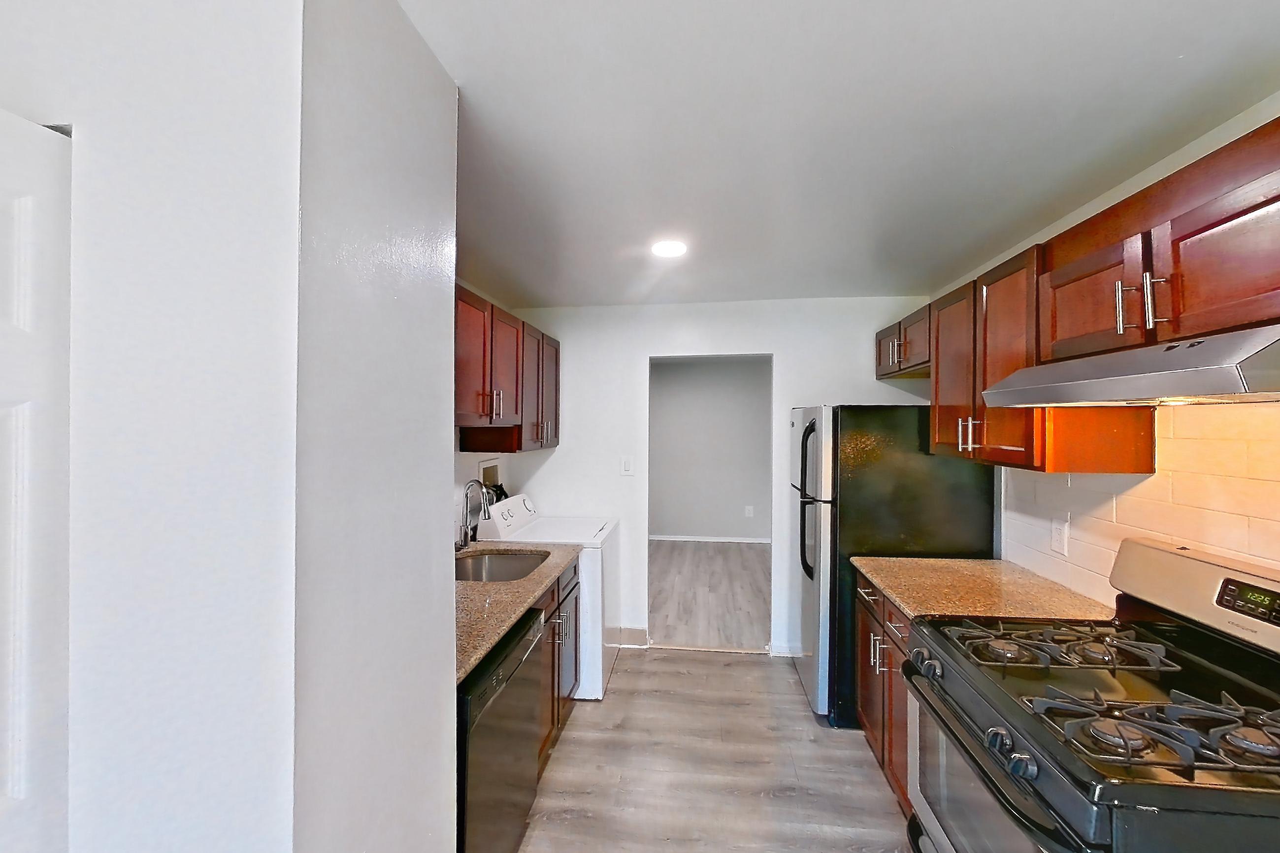 Kitchen with black appliances, dishwasher, gas range, in-unit laundry, light countertops, light stone countertops, light wood-finish flooring, oven/range, refrigerator, and stainless steel appliances, Apartment 9320ER33 at Franklin Park at Greenbelt Station