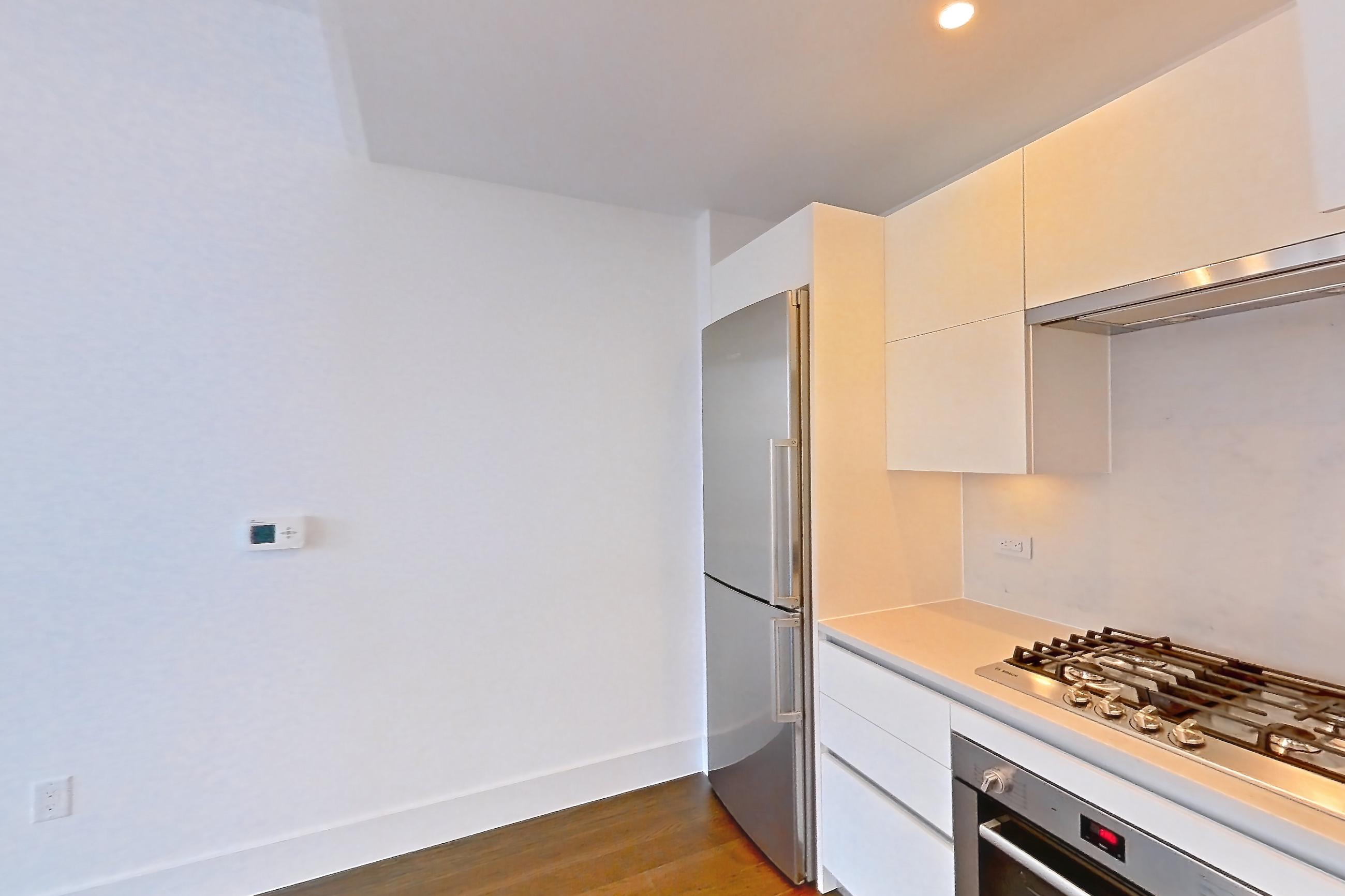 Kitchen with cooktop, dark wood-finish flooring, gas cooktop, light countertops, microwave, oven/range, refrigerator, stainless steel appliances, and white appliances, Apartment 38A at Summit NYC