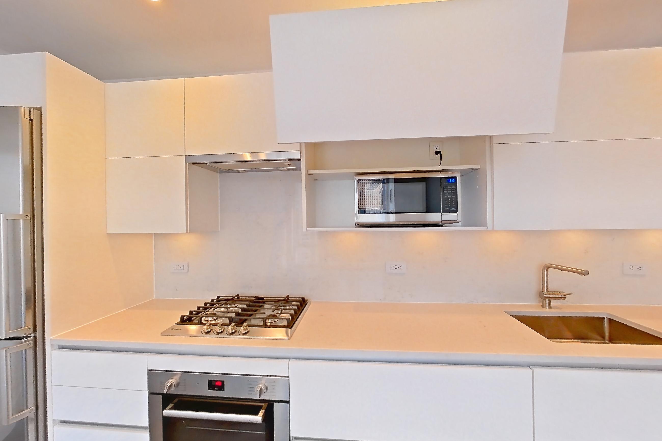 Kitchen with cooktop, dark wood-finish flooring, gas cooktop, light countertops, microwave, oven/range, refrigerator, stainless steel appliances, and white appliances, Apartment 38A at Summit NYC