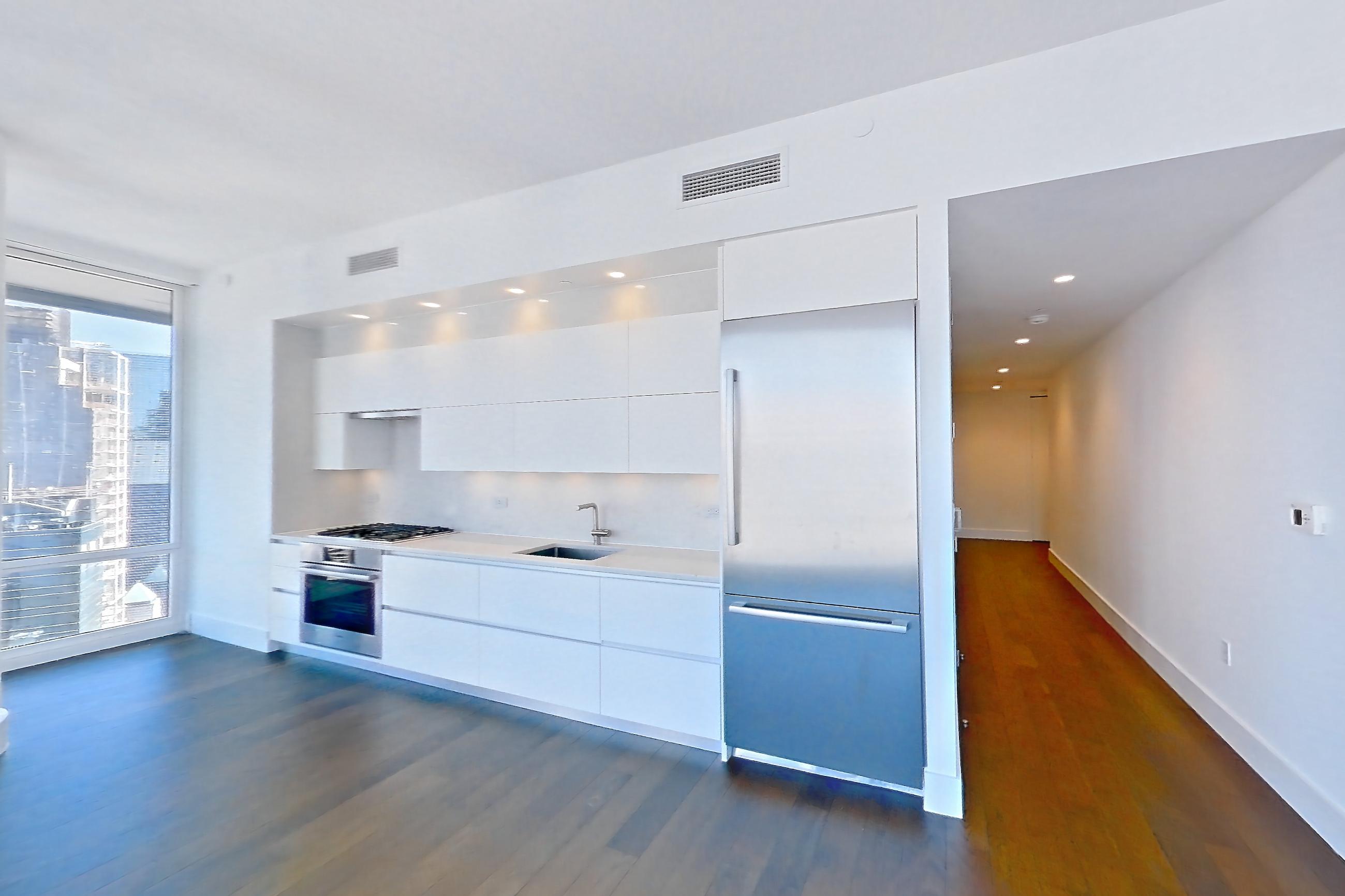 Living room with city view, cooktop, dark wood-finish flooring, gas cooktop, light countertops, oven/range, refrigerator, skyline view, stainless steel appliances, and wood-finish flooring, Apartment 35L at Summit NYC