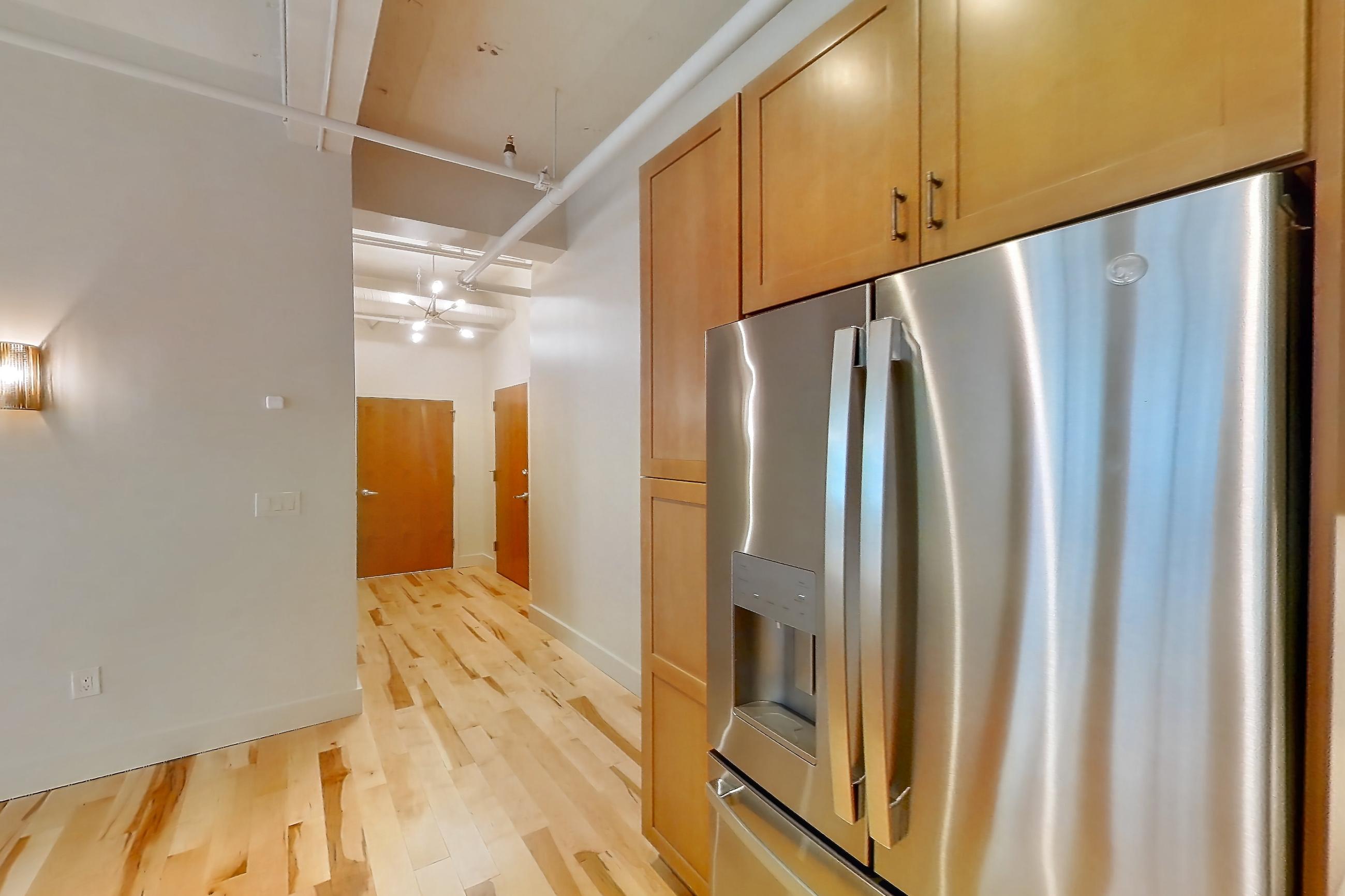 Kitchen with dishwasher, light countertops, light wood-finish flooring, oven/range, refrigerator, stainless steel appliances, and water & ice dispenser, Apartment 309 at Temple Building