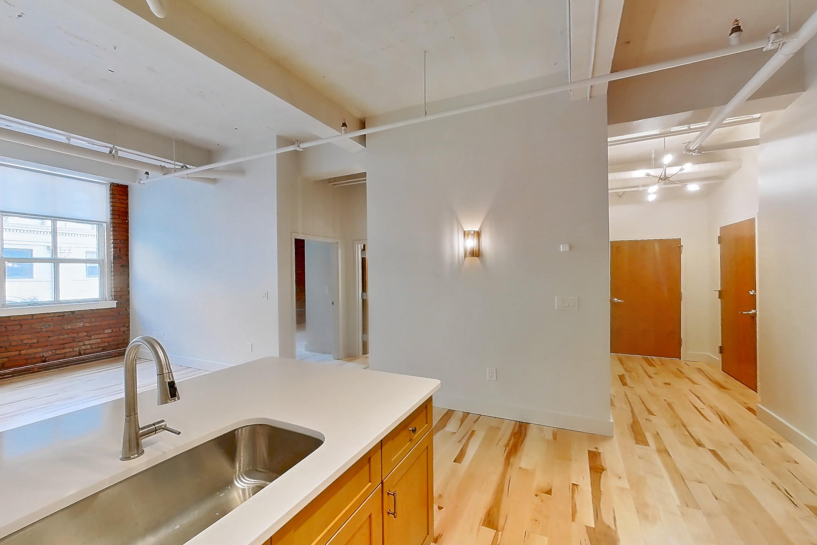 Kitchen with dishwasher, light countertops, light wood-finish flooring, oven/range, refrigerator, stainless steel appliances, and water & ice dispenser, Apartment 309 at Temple Building
