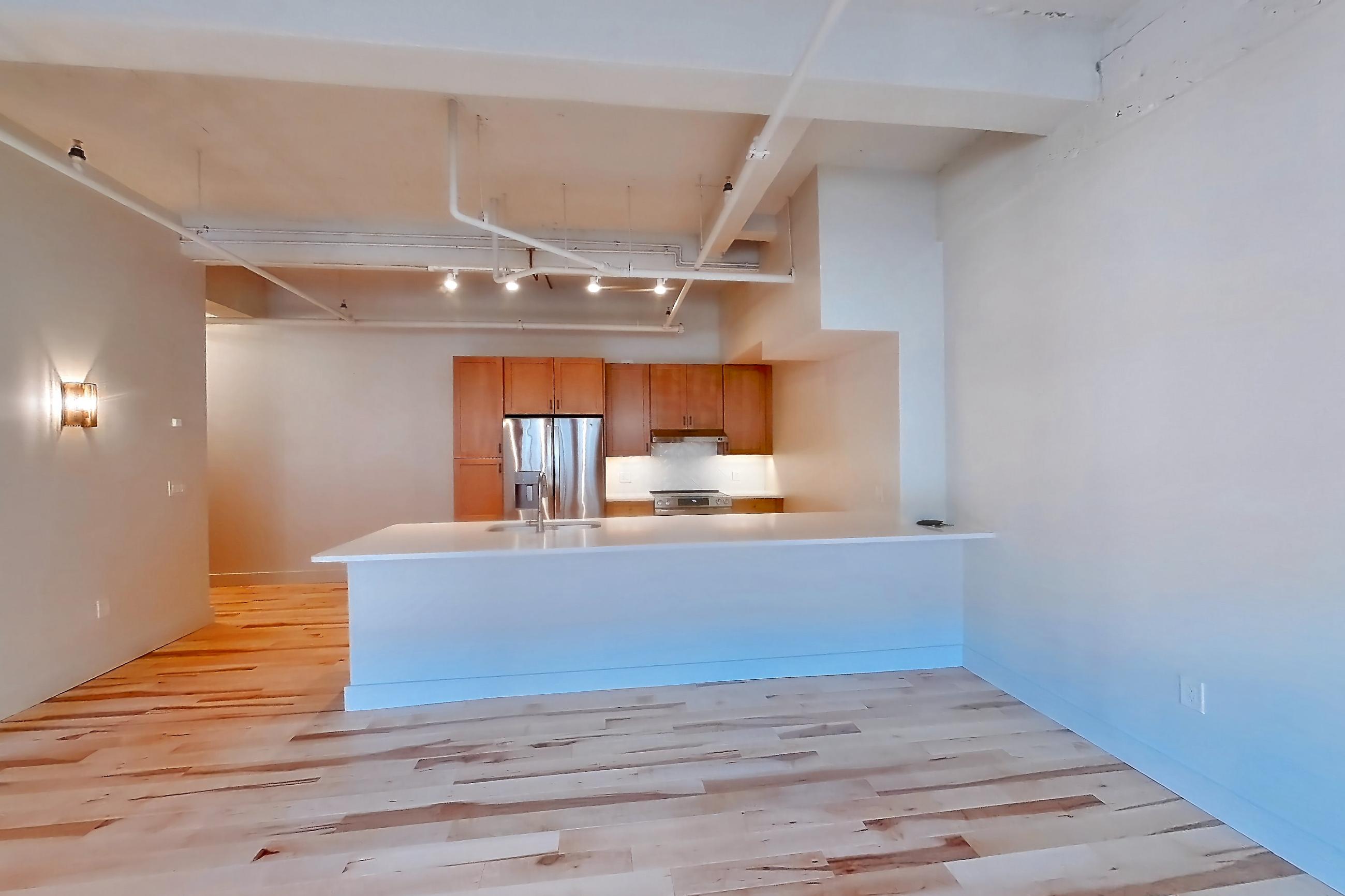 Living space with light countertops, light wood-finish flooring, oven/range, refrigerator, and stainless steel appliances, Apartment 309 at Temple Building