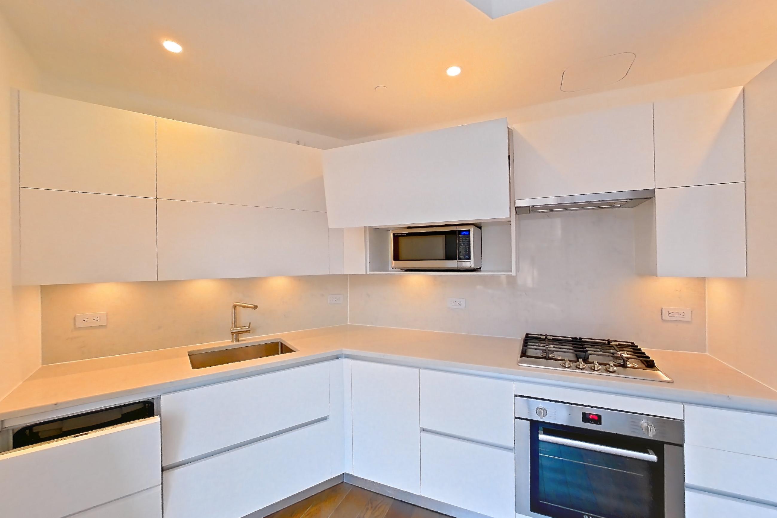 Kitchen with cooktop, dark wood-finish flooring, gas cooktop, light countertops, light stone countertops, microwave, oven/range, refrigerator, stainless steel appliances, and wood-finish flooring, Apartment 28M at Summit NYC