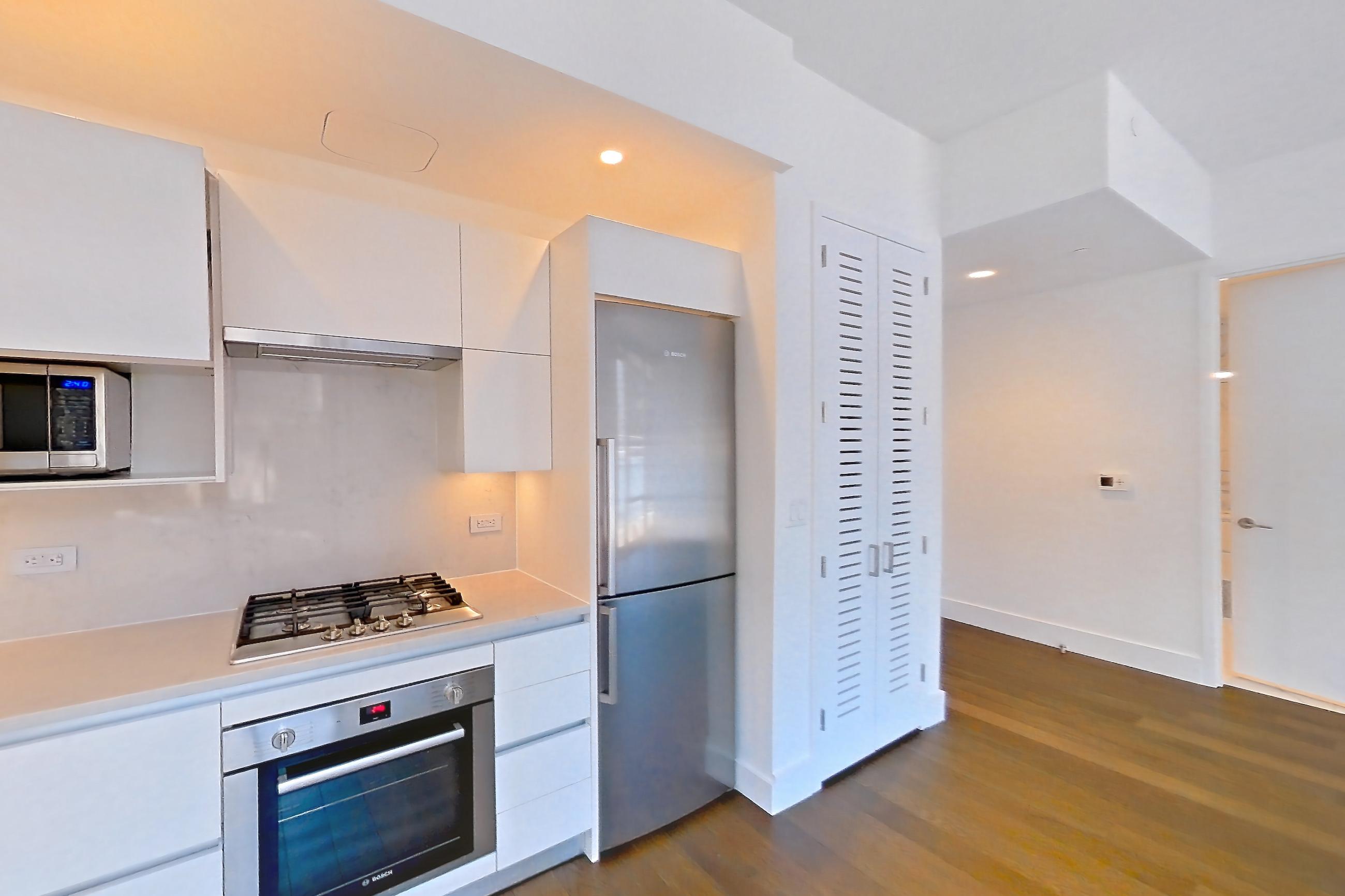 Kitchen with cooktop, dark wood-finish flooring, gas cooktop, light countertops, light stone countertops, microwave, oven/range, refrigerator, stainless steel appliances, and wood-finish flooring, Apartment 28M at Summit NYC