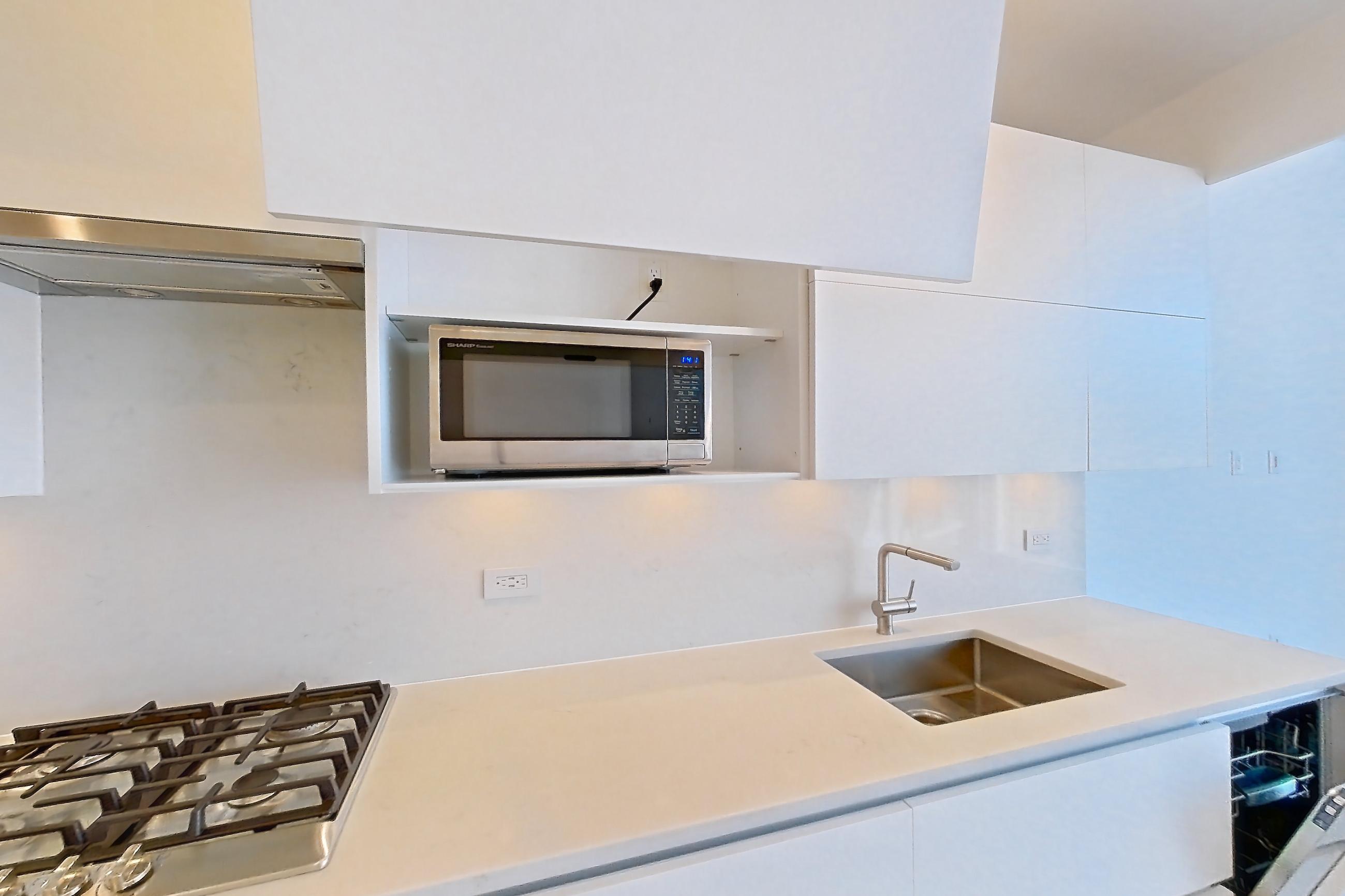 Kitchen with cooktop, dark wood-finish flooring, dishwasher, gas cooktop, light countertops, light stone countertops, microwave, oven/range, refrigerator, skyline view, stainless steel appliances, and wood-finish flooring, Apartment 38C at Summit NYC
