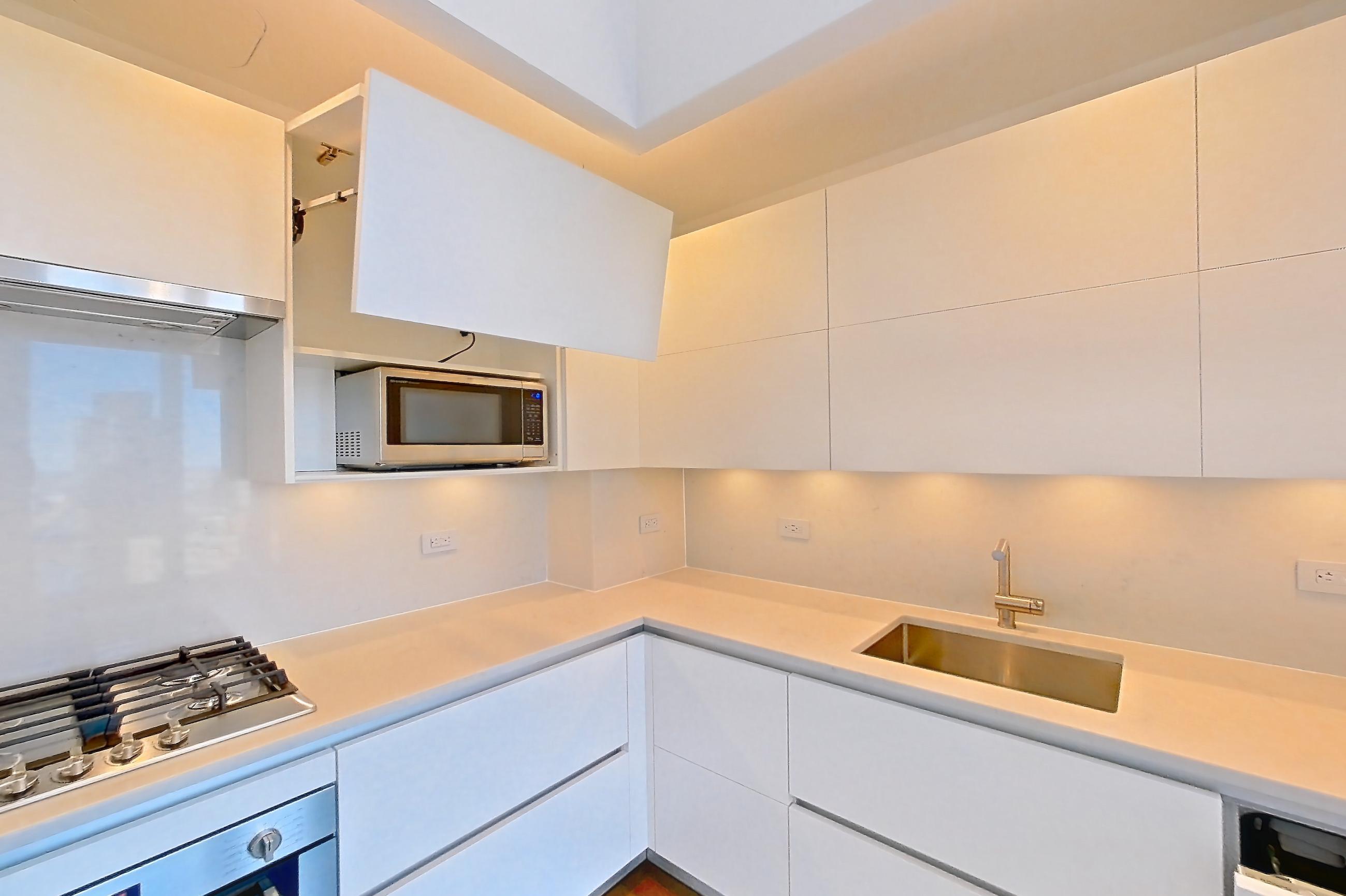 Kitchen with cooktop, dark wood-finish flooring, gas cooktop, light countertops, microwave, oven/range, refrigerator, stainless steel appliances, and wood-finish flooring, Apartment 38J at Summit NYC
