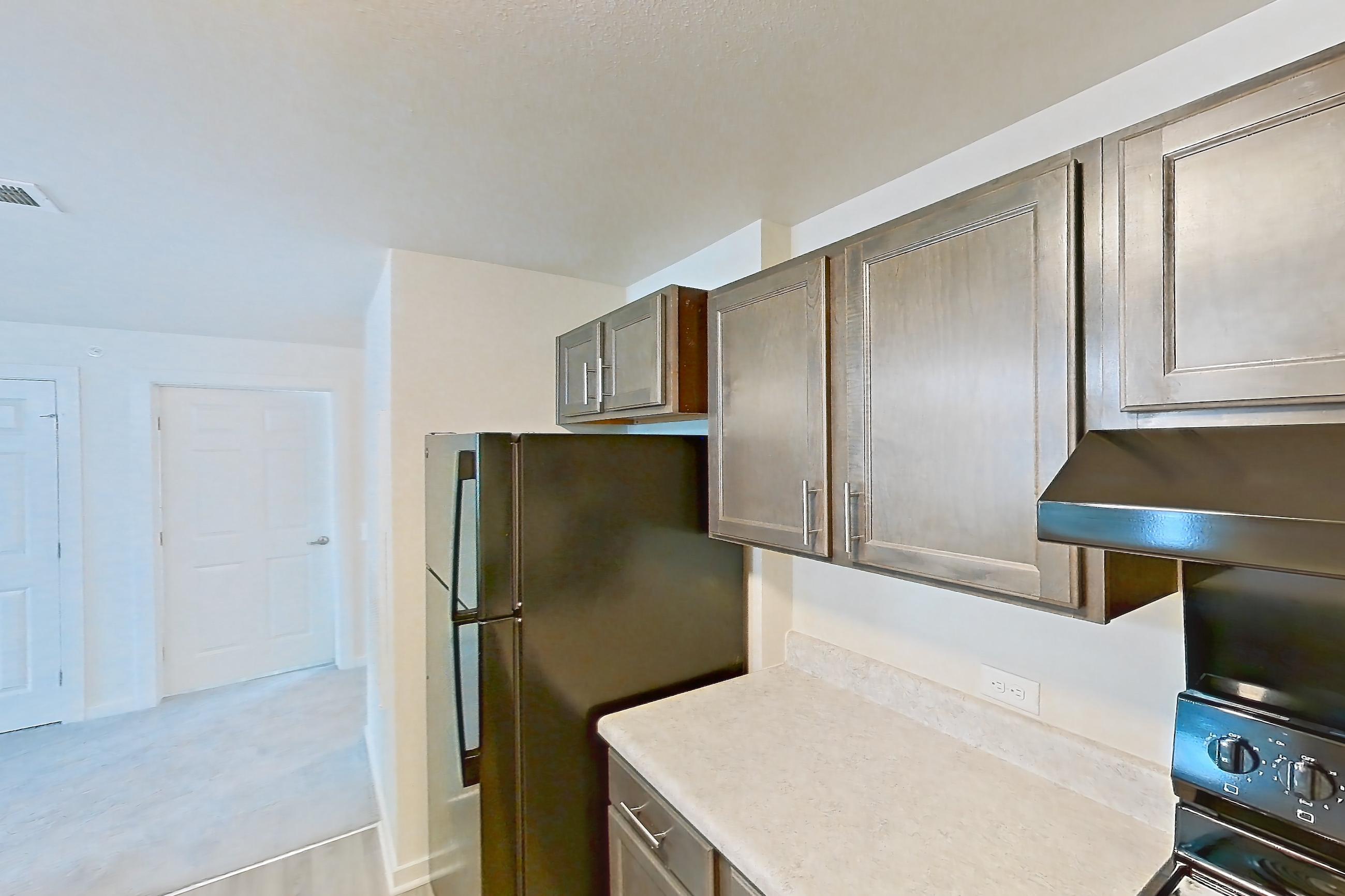 Kitchen with black appliances, dishwasher, electric range, light countertops, light wood-finish flooring, oven/range, range hood, refrigerator, and stainless steel appliances, Apartment 8O at The Creek at Cottonwood