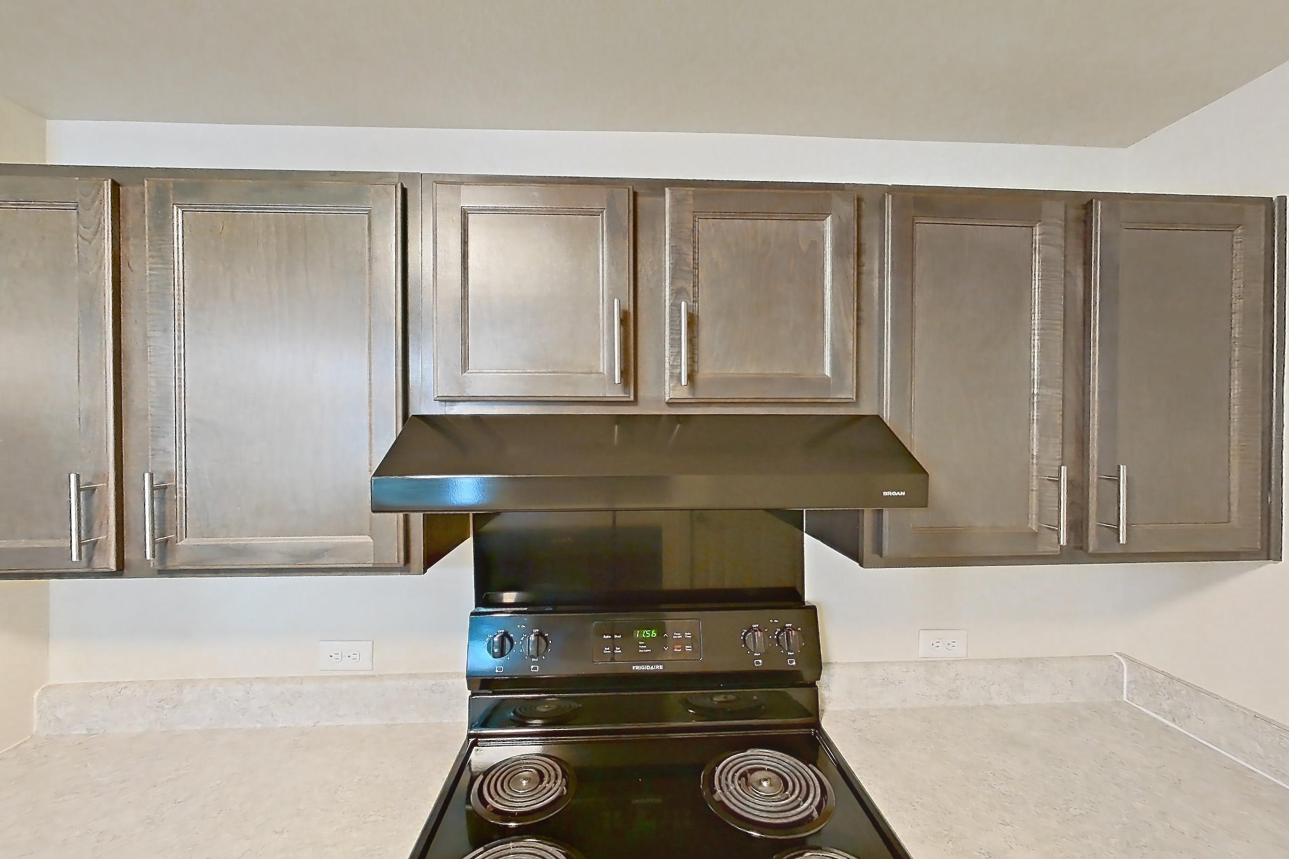 Kitchen with black appliances, dishwasher, electric range, light countertops, light wood-finish flooring, oven/range, range hood, refrigerator, and stainless steel appliances, Apartment 8O at The Creek at Cottonwood