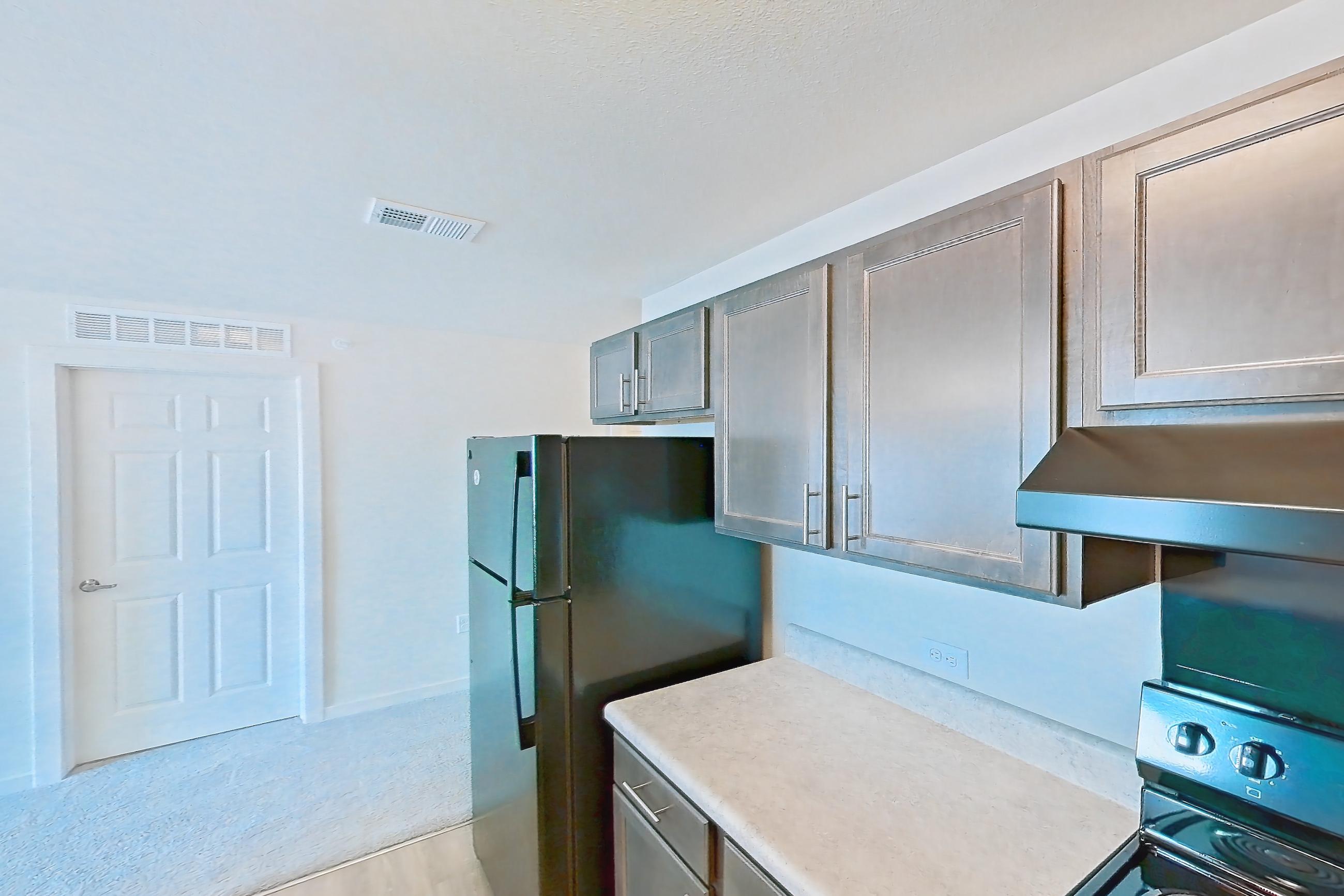 Kitchen with black appliances, dishwasher, electric range, light countertops, light wood-finish flooring, oven/range, range hood, refrigerator, and stainless steel appliances, Apartment 4Q at The Creek at Cottonwood