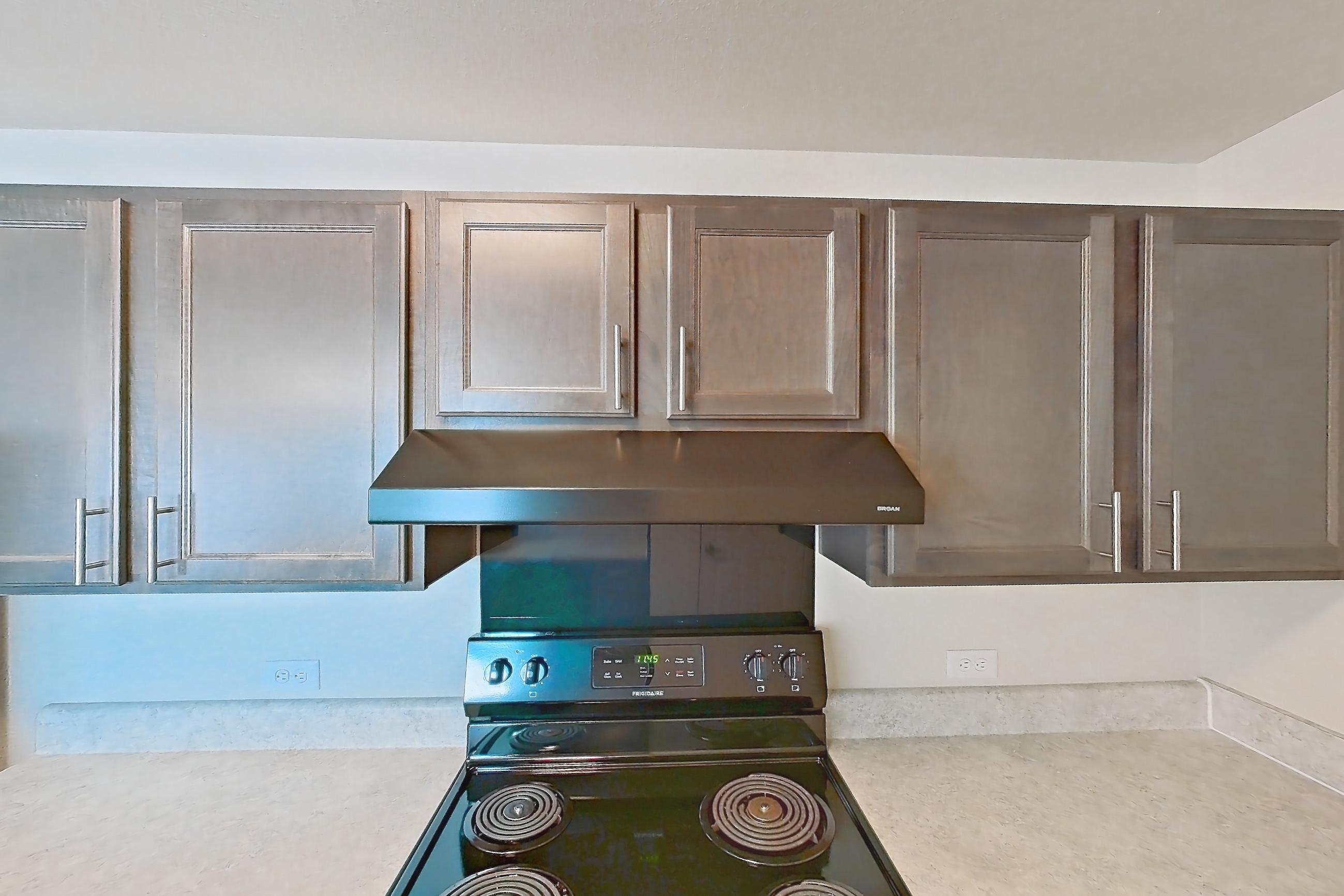 Kitchen with black appliances, dishwasher, electric range, light countertops, light wood-finish flooring, oven/range, range hood, refrigerator, and stainless steel appliances, Apartment 4Q at The Creek at Cottonwood