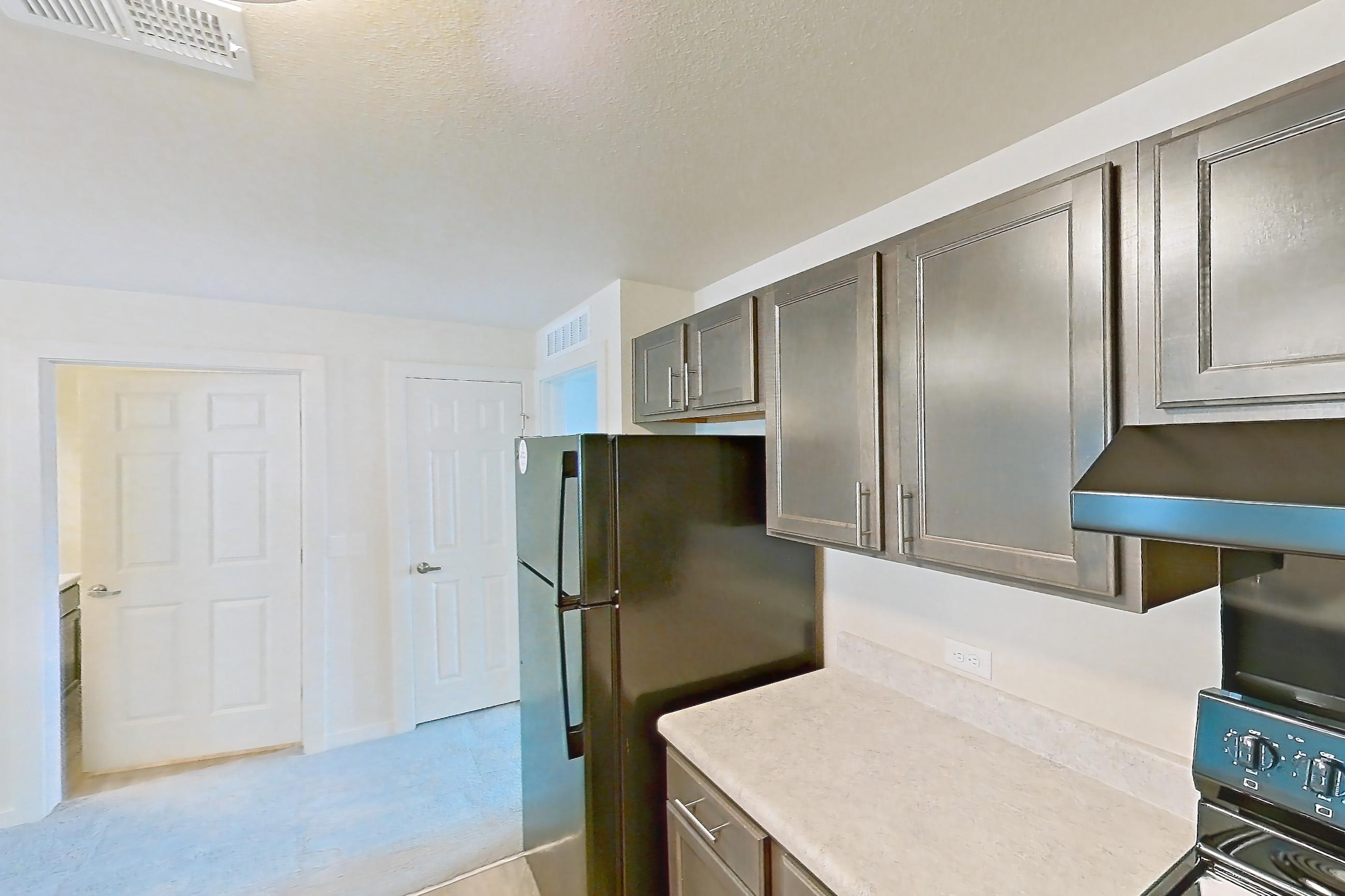 Kitchen with black appliances, dishwasher, electric range, light countertops, light wood-finish flooring, oven/range, range hood, refrigerator, and stainless steel appliances, Apartment 2D at The Creek at Cottonwood