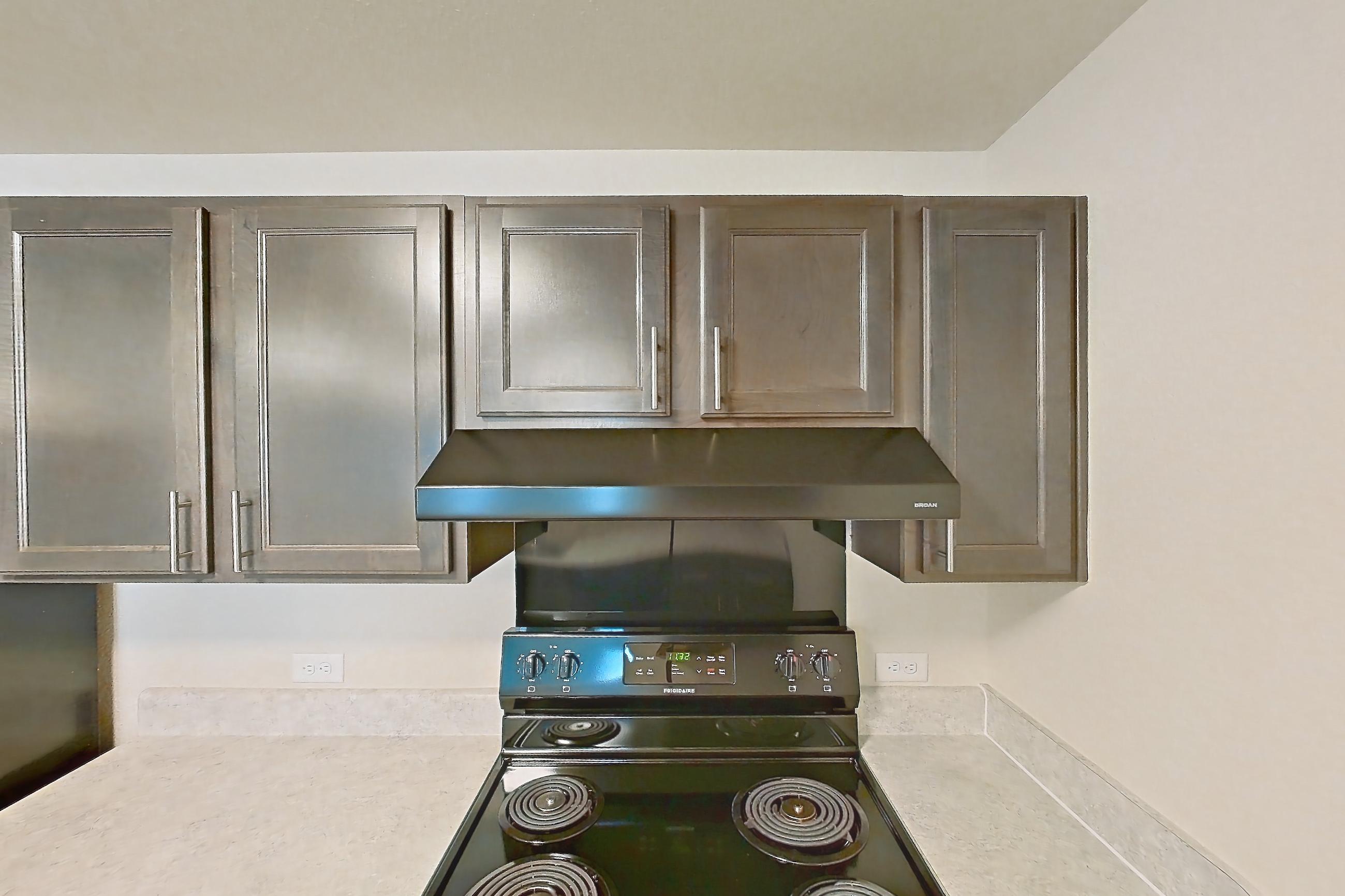 Kitchen with black appliances, dishwasher, electric range, light countertops, light wood-finish flooring, oven/range, range hood, refrigerator, and stainless steel appliances, Apartment 2D at The Creek at Cottonwood