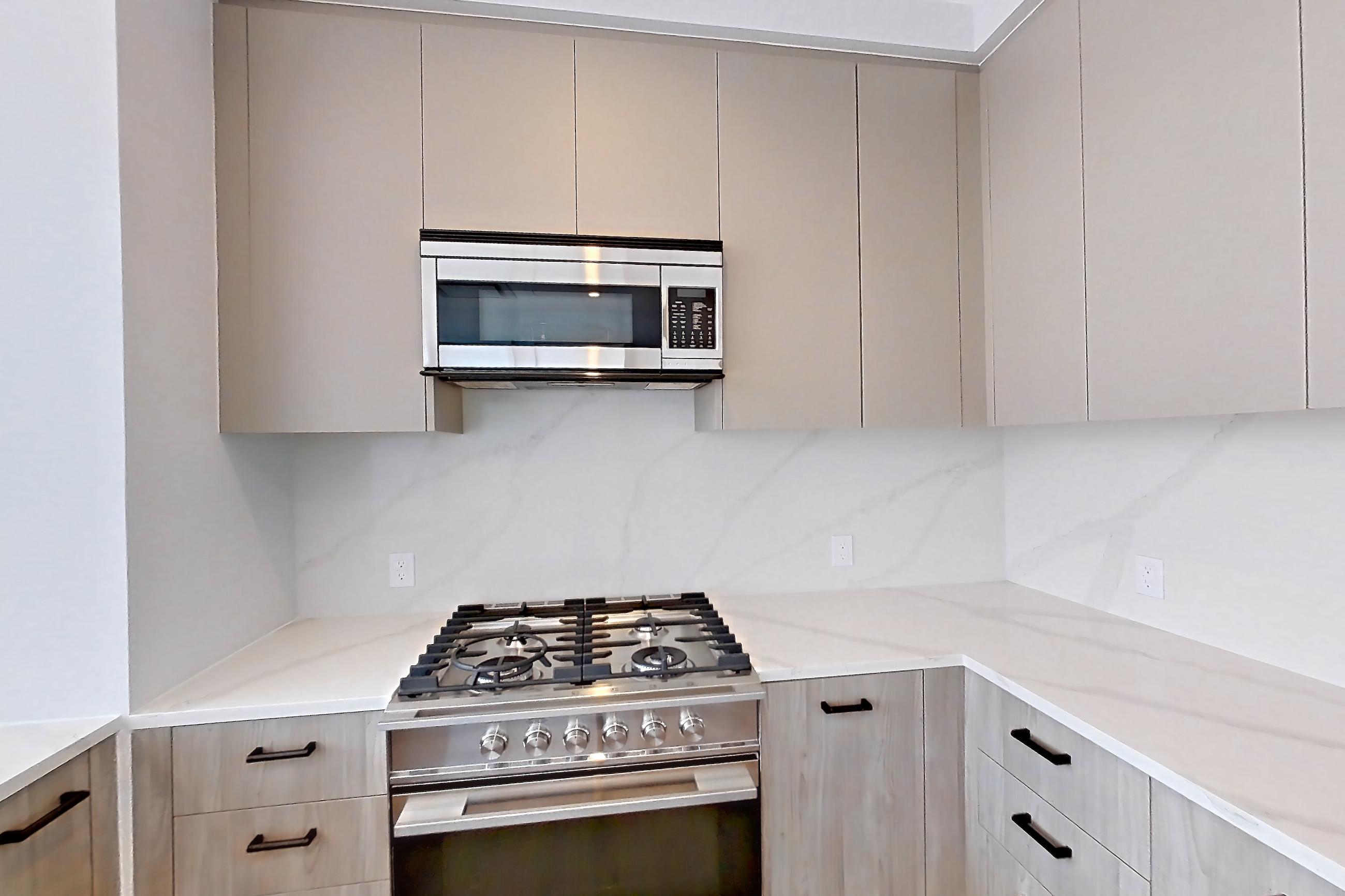 Kitchen with gas range, light countertops, light stone countertops, light wood-finish flooring, microwave, oven/range, and stainless steel appliances, Apartment PH3C at Lumen