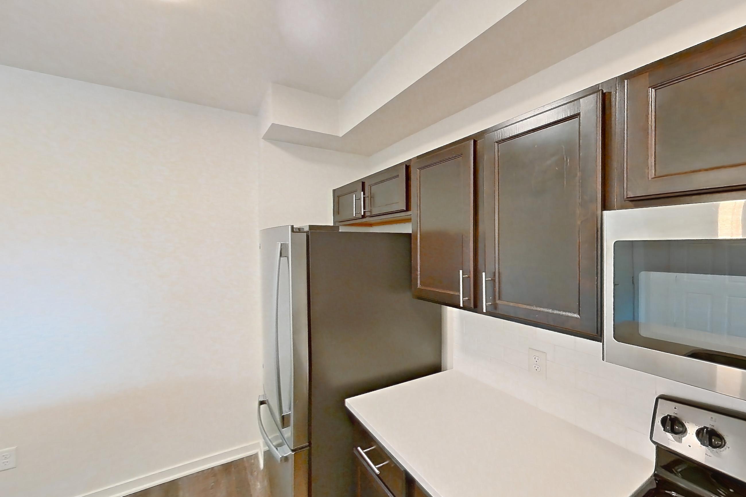 Kitchen with black appliances, dark wood-finish flooring, dishwasher, electric range, light countertops, microwave, oven/range, refrigerator, and stainless steel appliances, Apartment 3204 at Village at Thorncreek