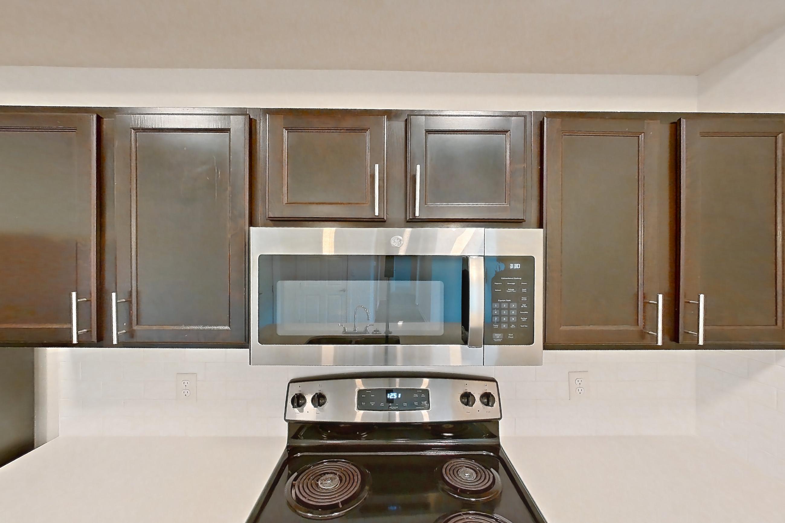 Kitchen with black appliances, dark wood-finish flooring, dishwasher, electric range, light countertops, microwave, oven/range, refrigerator, and stainless steel appliances, Apartment 3204 at Village at Thorncreek