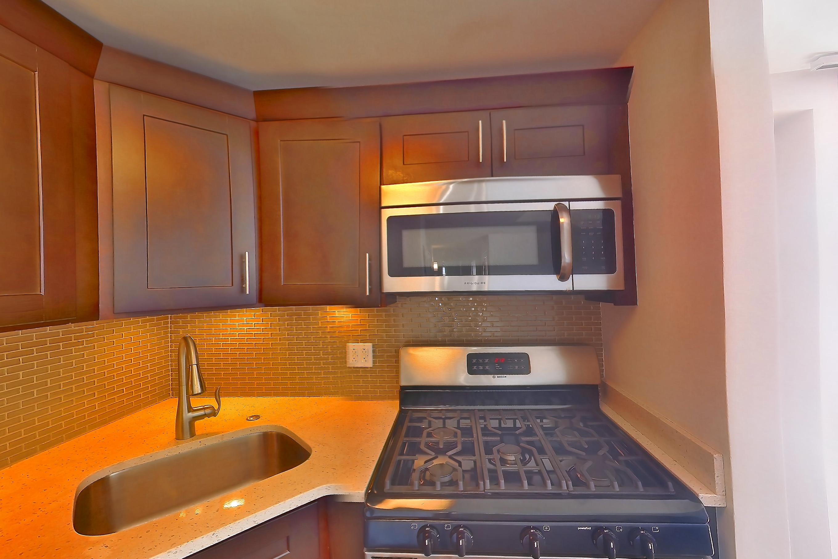 Kitchen with dark wood-finish flooring, dishwasher, gas range, light countertops, light stone countertops, microwave, oven/range, refrigerator, stainless steel appliances, and white appliances, Apartment 1401 at Stonehenge Leasing
