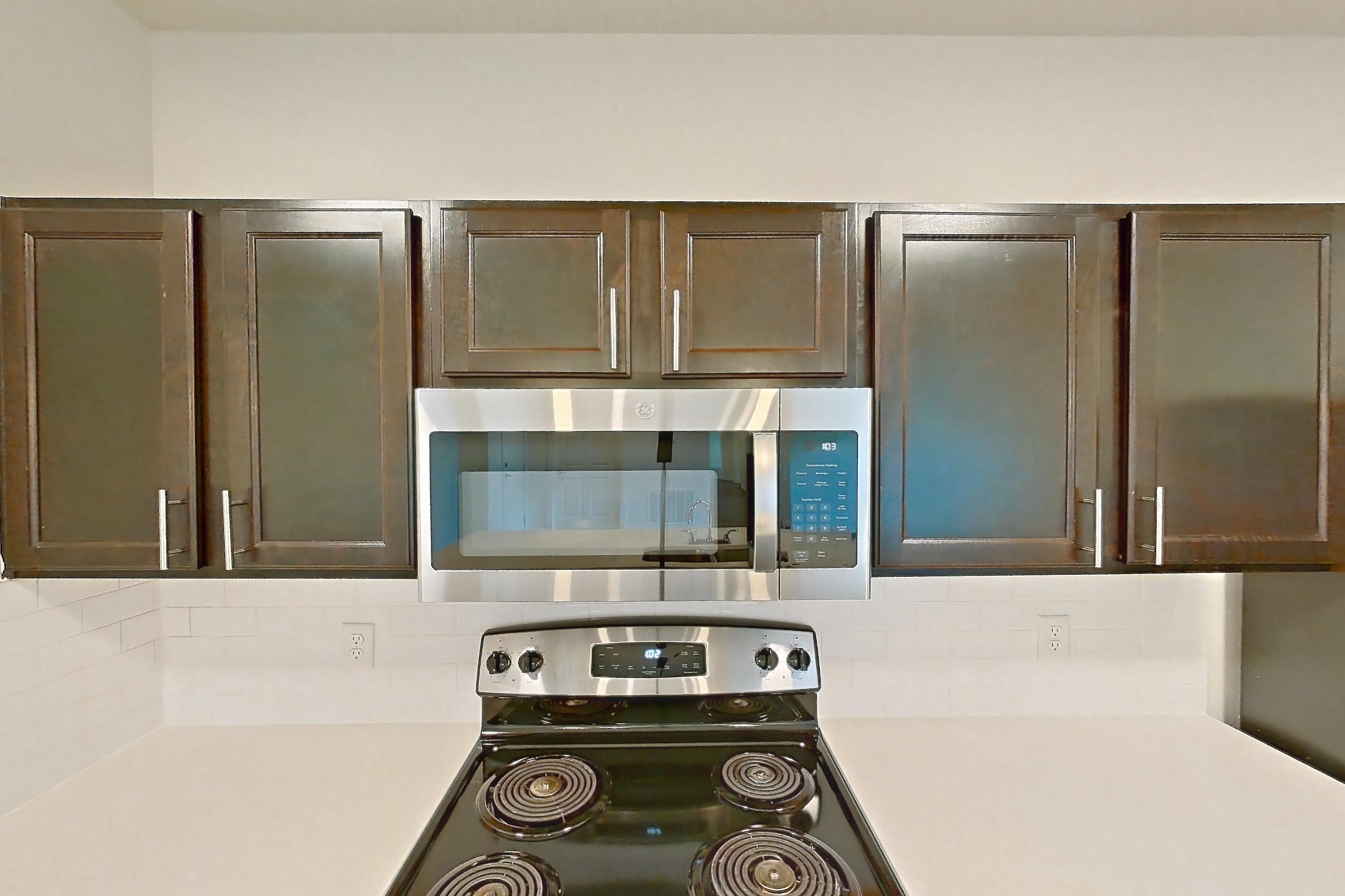 Kitchen with black appliances, dark wood-finish flooring, dishwasher, electric range, light countertops, microwave, oven/range, refrigerator, and stainless steel appliances, Apartment 3205 at Village at Thorncreek