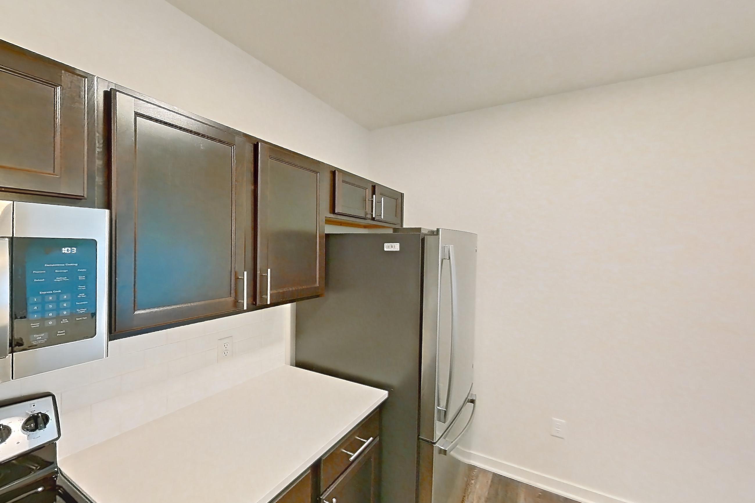 Kitchen with black appliances, dark wood-finish flooring, dishwasher, electric range, light countertops, microwave, oven/range, refrigerator, and stainless steel appliances, Apartment 3205 at Village at Thorncreek