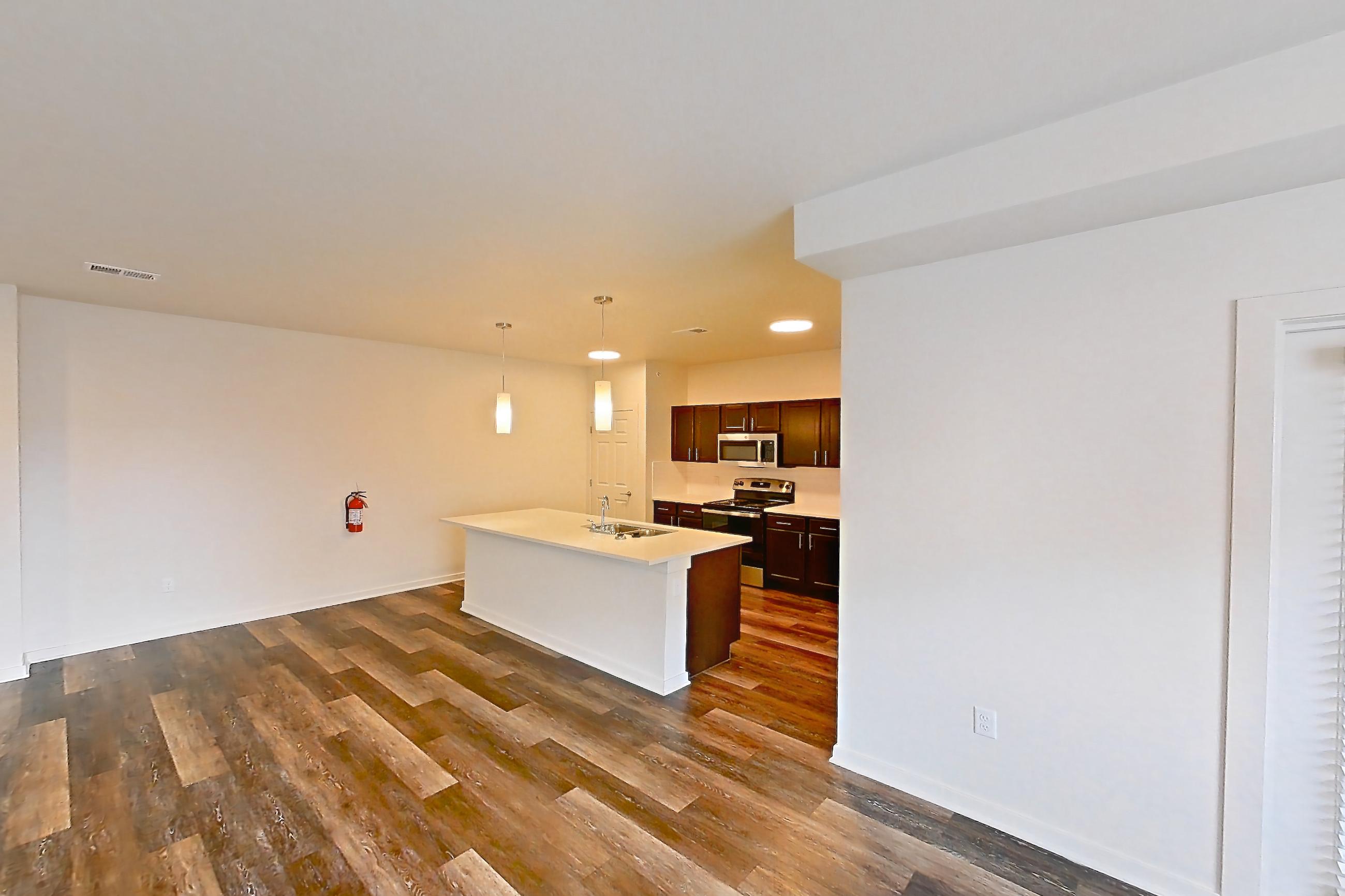Living space with dark wood-finish flooring, electric range, kitchen island, light countertops, oven/range, and stainless steel appliances, Apartment 3205 at Village at Thorncreek