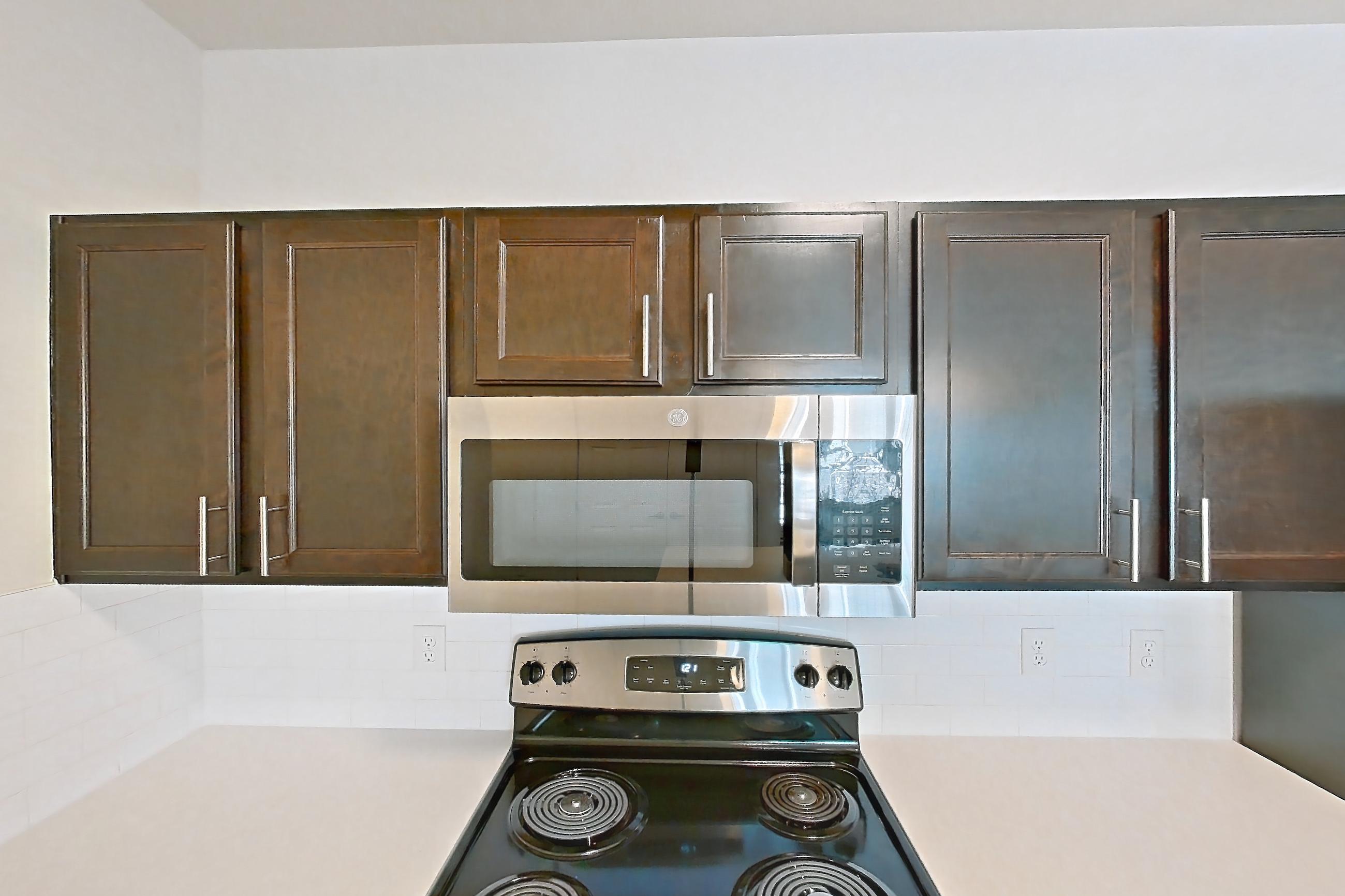 Kitchen with black appliances, dark wood-finish flooring, dishwasher, electric range, light countertops, microwave, oven/range, refrigerator, and stainless steel appliances, Apartment 11201 at Village at Thorncreek