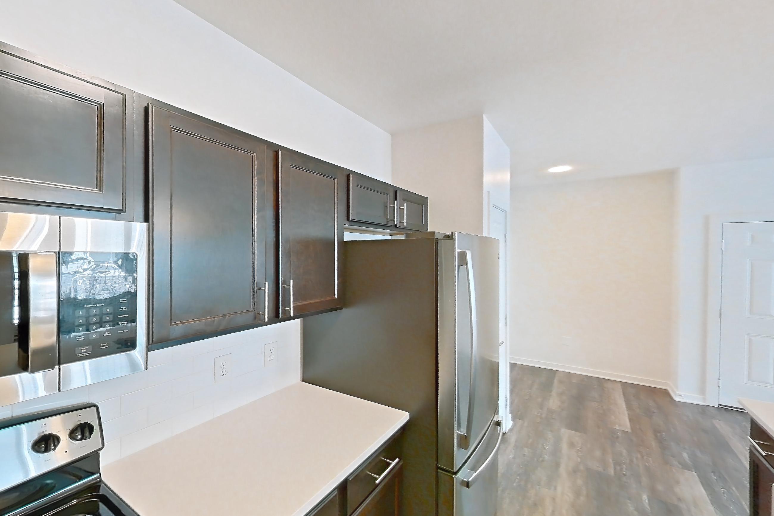 Kitchen with black appliances, dark wood-finish flooring, dishwasher, electric range, light countertops, microwave, oven/range, refrigerator, and stainless steel appliances, Apartment 11201 at Village at Thorncreek