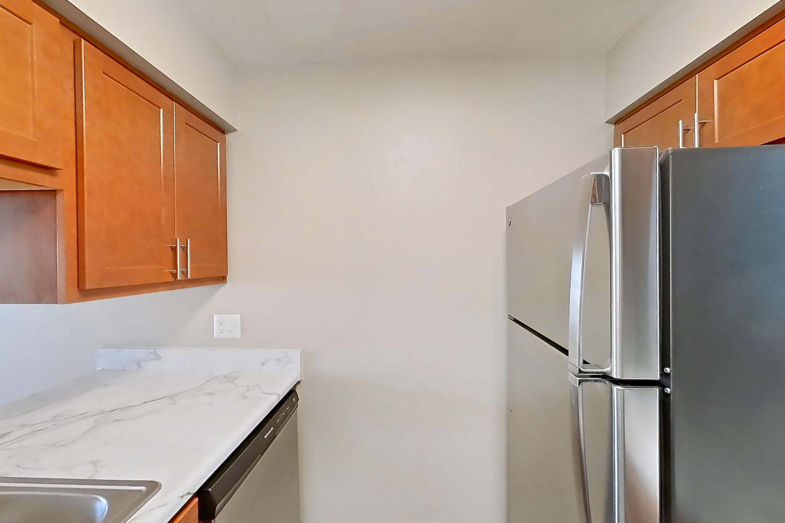 Kitchen with dark wood-finish flooring, dishwasher, electric range, light countertops, light stone countertops, oven/range, range hood, refrigerator, and stainless steel appliances, Apartment 4060 Unit 11 at Aaron Lake Apartments