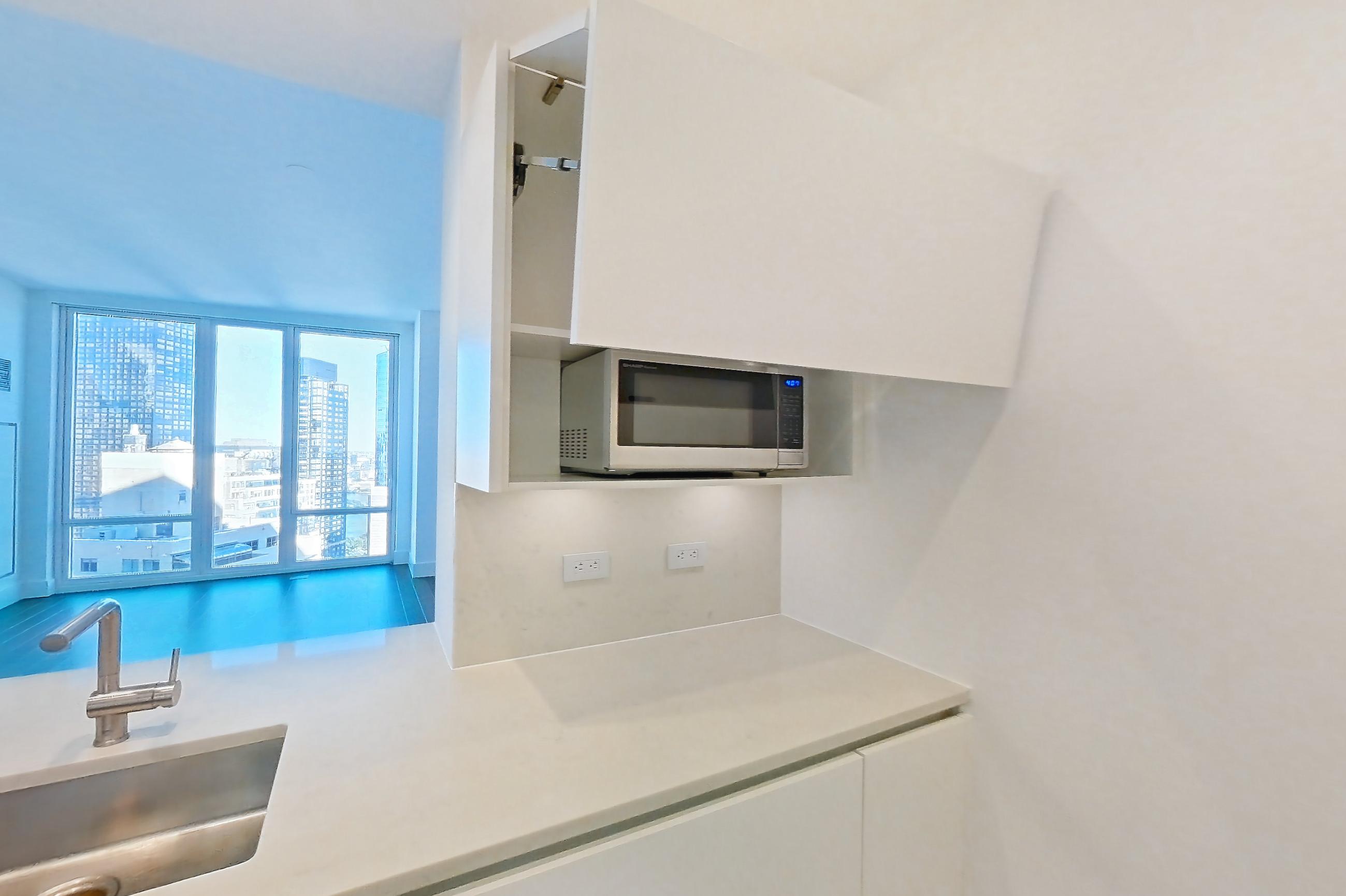Kitchen with baseboard heating, cooktop, dark wood-finish flooring, gas cooktop, light countertops, light stone countertops, microwave, and stainless steel appliances, Apartment 33k at Summit NYC