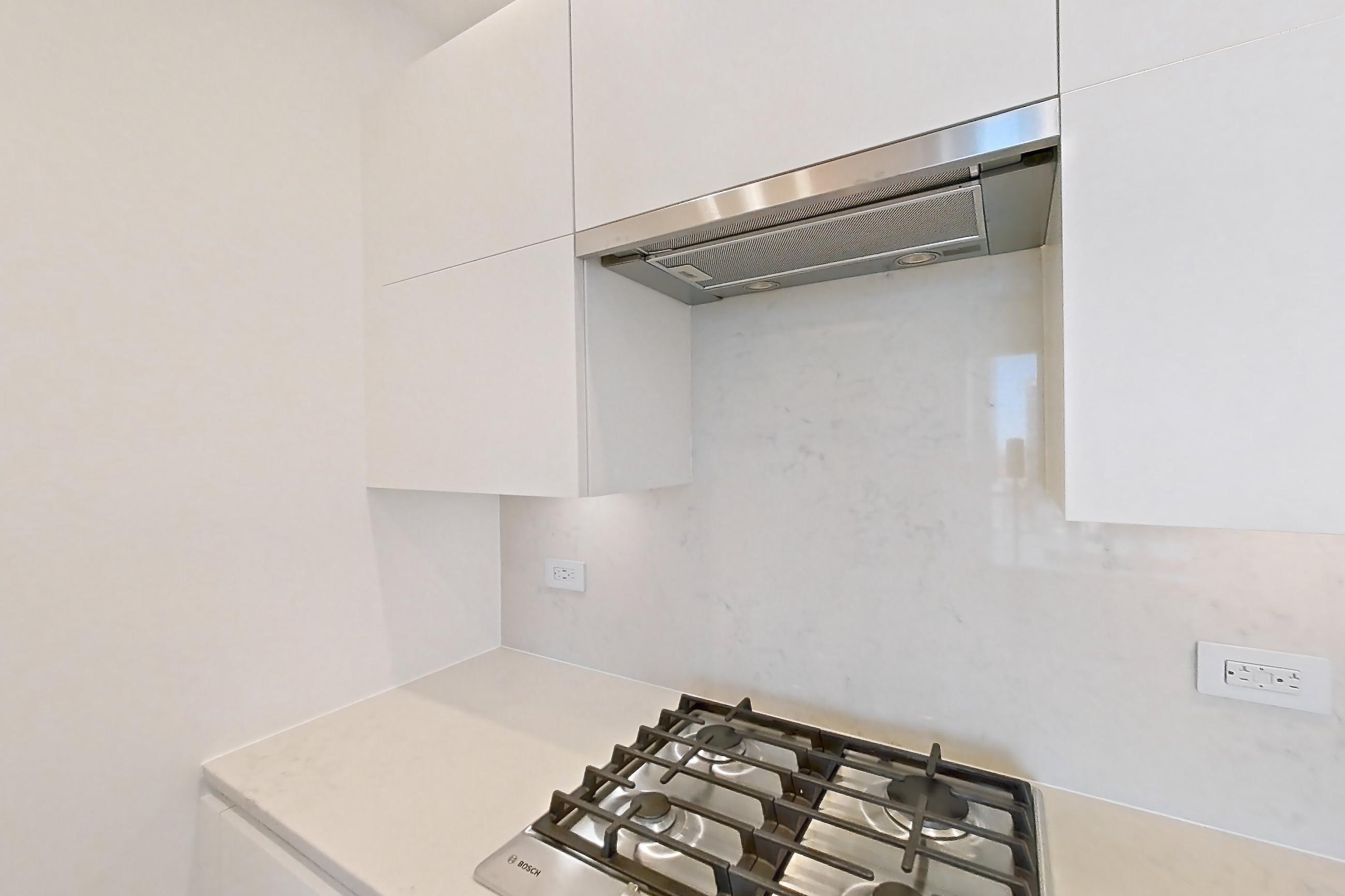 Kitchen with baseboard heating, cooktop, dark wood-finish flooring, gas cooktop, light countertops, light stone countertops, microwave, and stainless steel appliances, Apartment 33k at Summit NYC