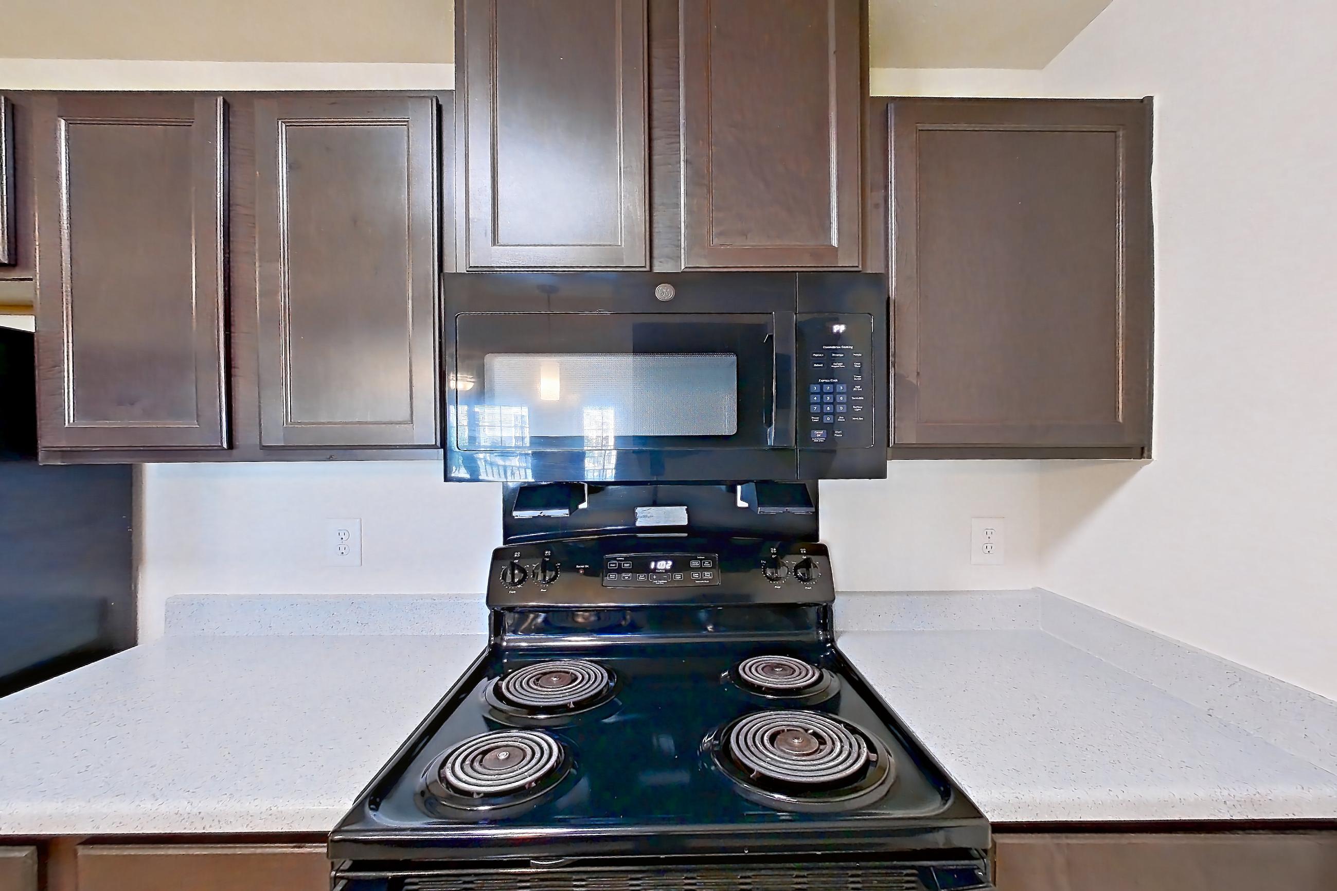 Kitchen with black appliances, dishwasher, electric range, light countertops, light stone countertops, light wood-finish flooring, microwave, oven/range, and refrigerator, Apartment 7206 at Ivy Ridge