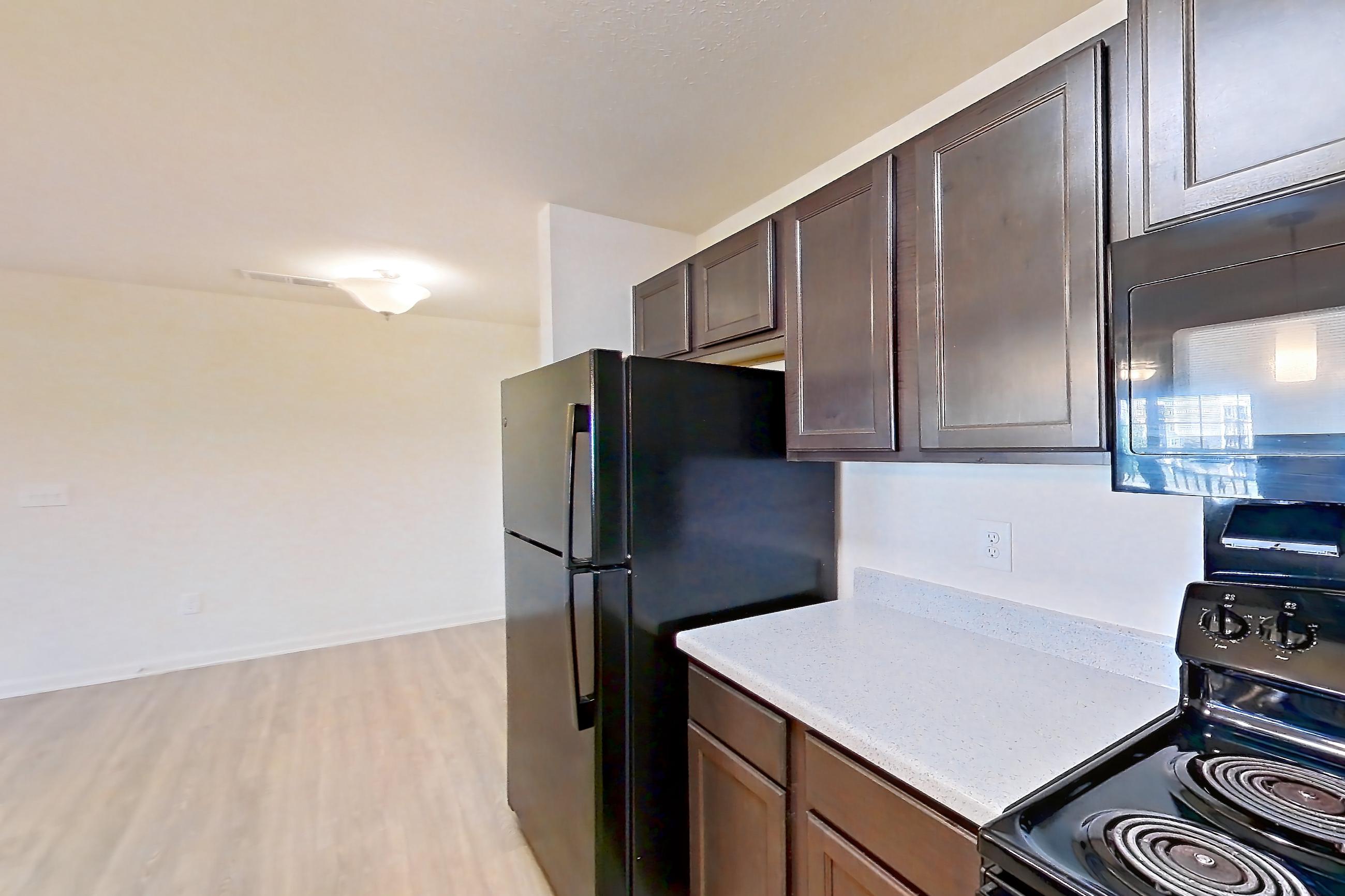 Kitchen with black appliances, dishwasher, electric range, light countertops, light stone countertops, light wood-finish flooring, microwave, oven/range, and refrigerator, Apartment 7206 at Ivy Ridge