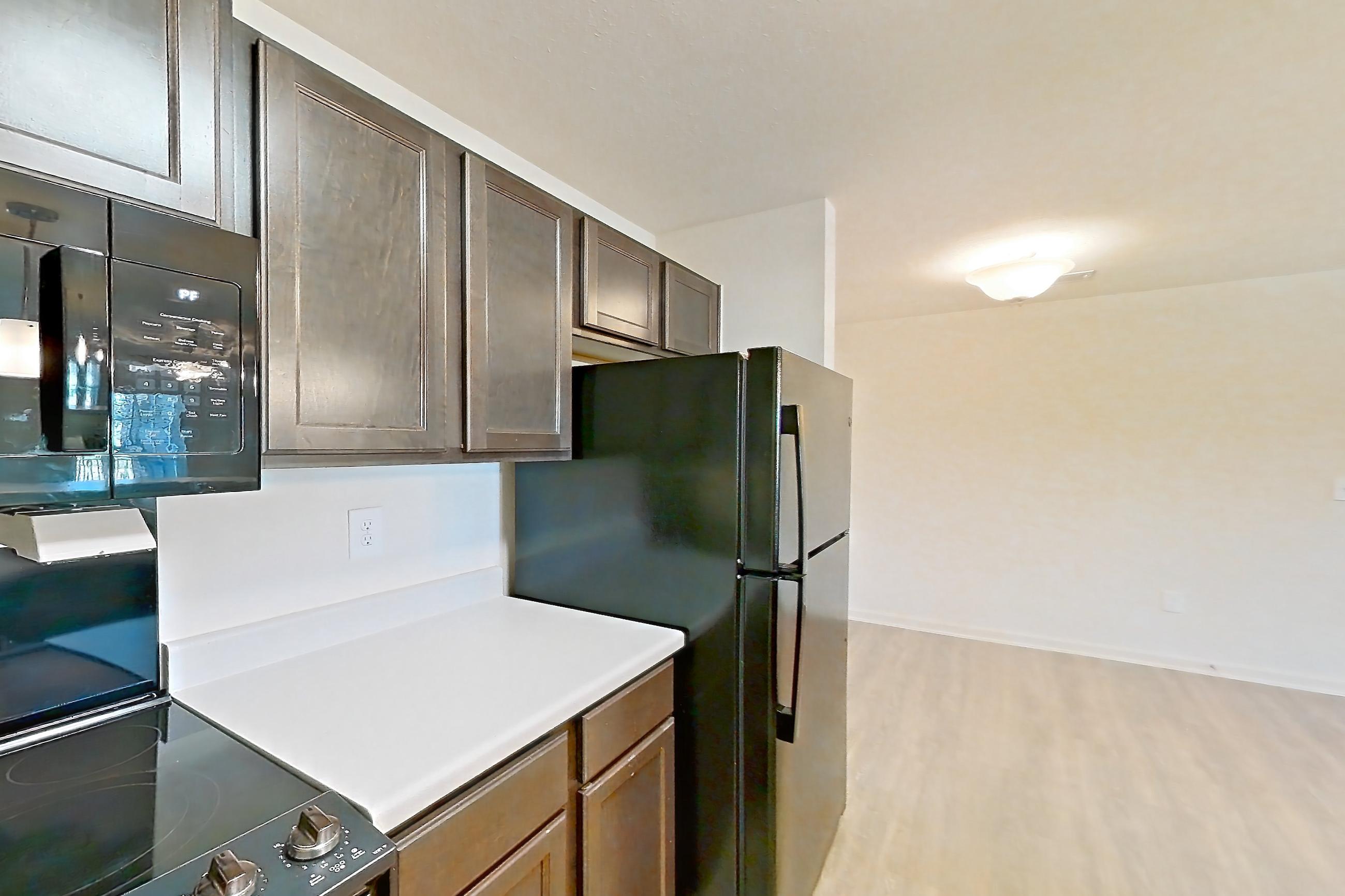 Kitchen with black appliances, electric range, light countertops, light wood-finish flooring, microwave, oven/range, refrigerator, and stainless steel appliances, Apartment 10201 at Ivy Ridge