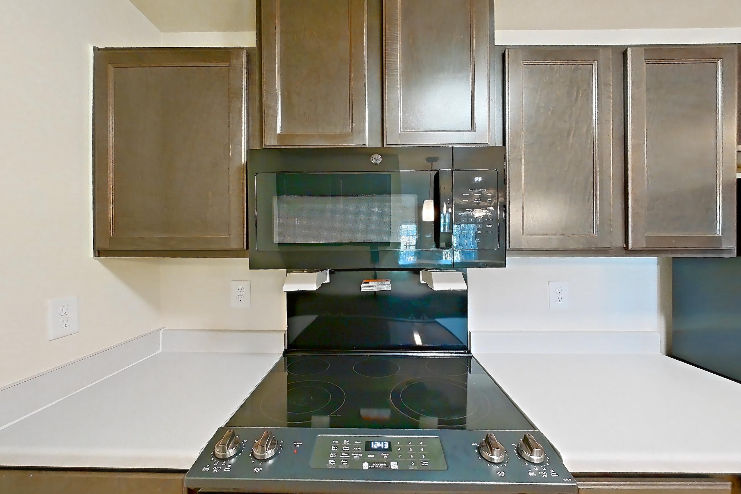 Kitchen with black appliances, electric range, light countertops, light wood-finish flooring, microwave, oven/range, refrigerator, and stainless steel appliances, Apartment 10201 at Ivy Ridge