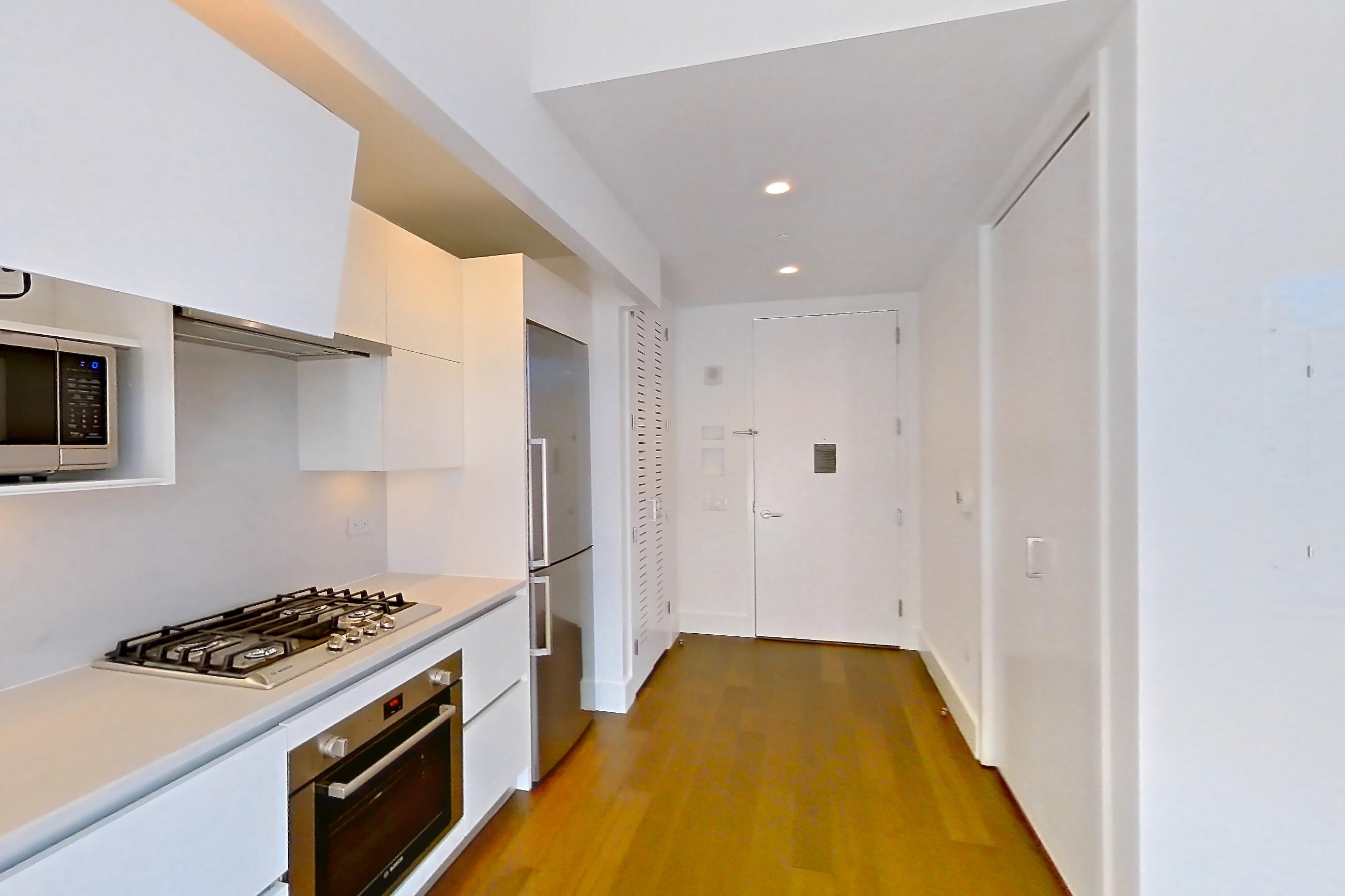 Kitchen with cooktop, dark wood-finish flooring, gas cooktop, light countertops, microwave, oven/range, refrigerator, stainless steel appliances, and white appliances, Apartment 40M at Summit NYC