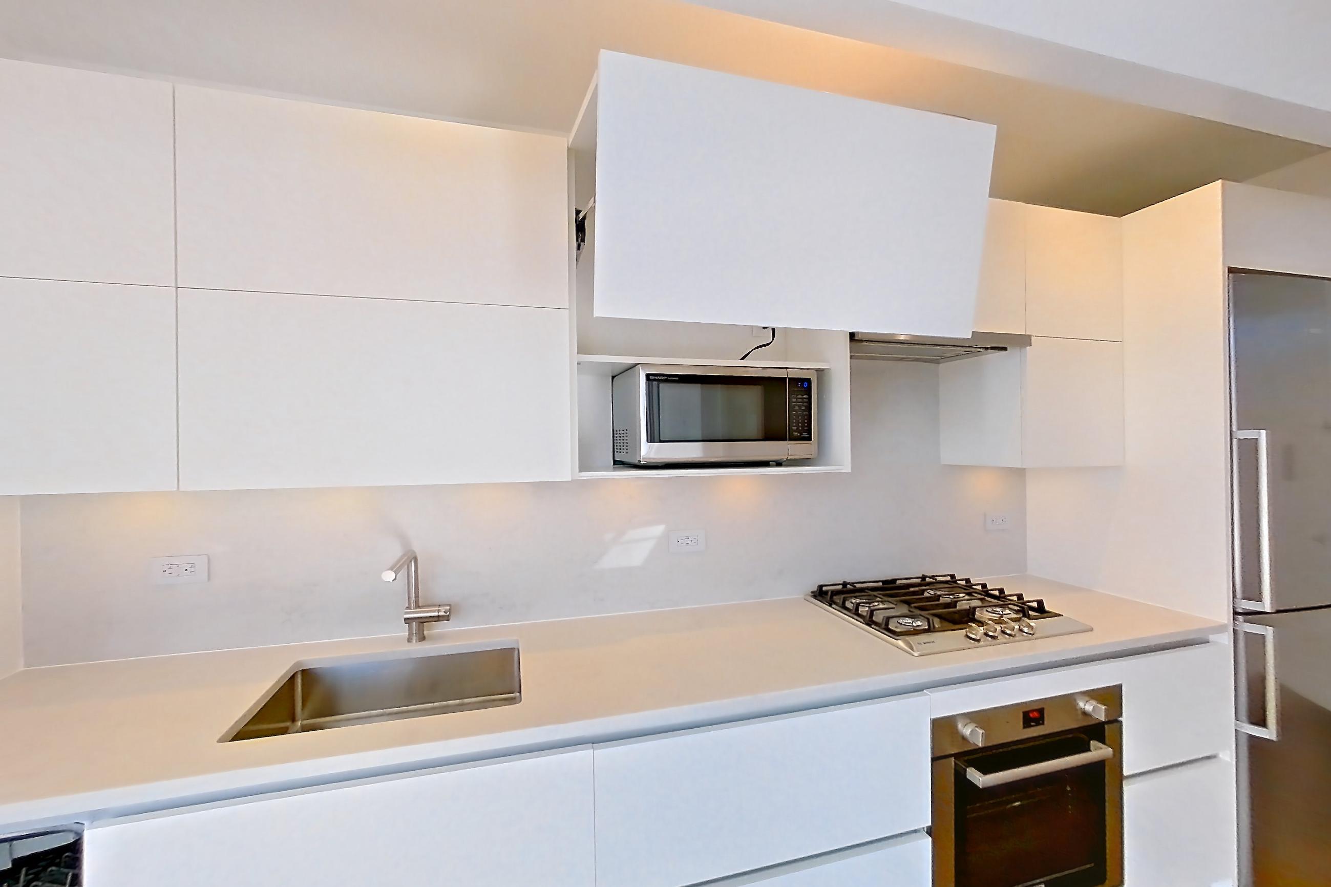 Kitchen with cooktop, dark wood-finish flooring, gas cooktop, light countertops, microwave, oven/range, refrigerator, stainless steel appliances, and white appliances, Apartment 40M at Summit NYC