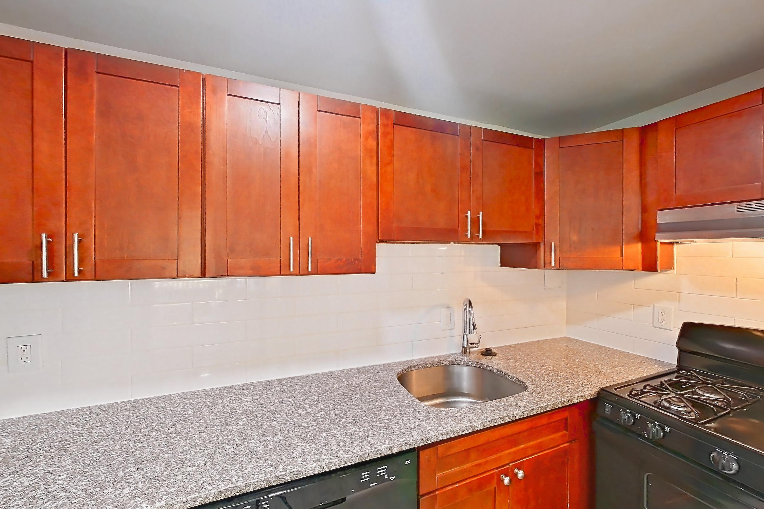 Kitchen with black appliances, dishwasher, gas range, light countertops, light stone countertops, light wood-finish flooring, oven/range, refrigerator, and stainless steel appliances, Apartment 9110ER22 at Franklin Park at Greenbelt Station