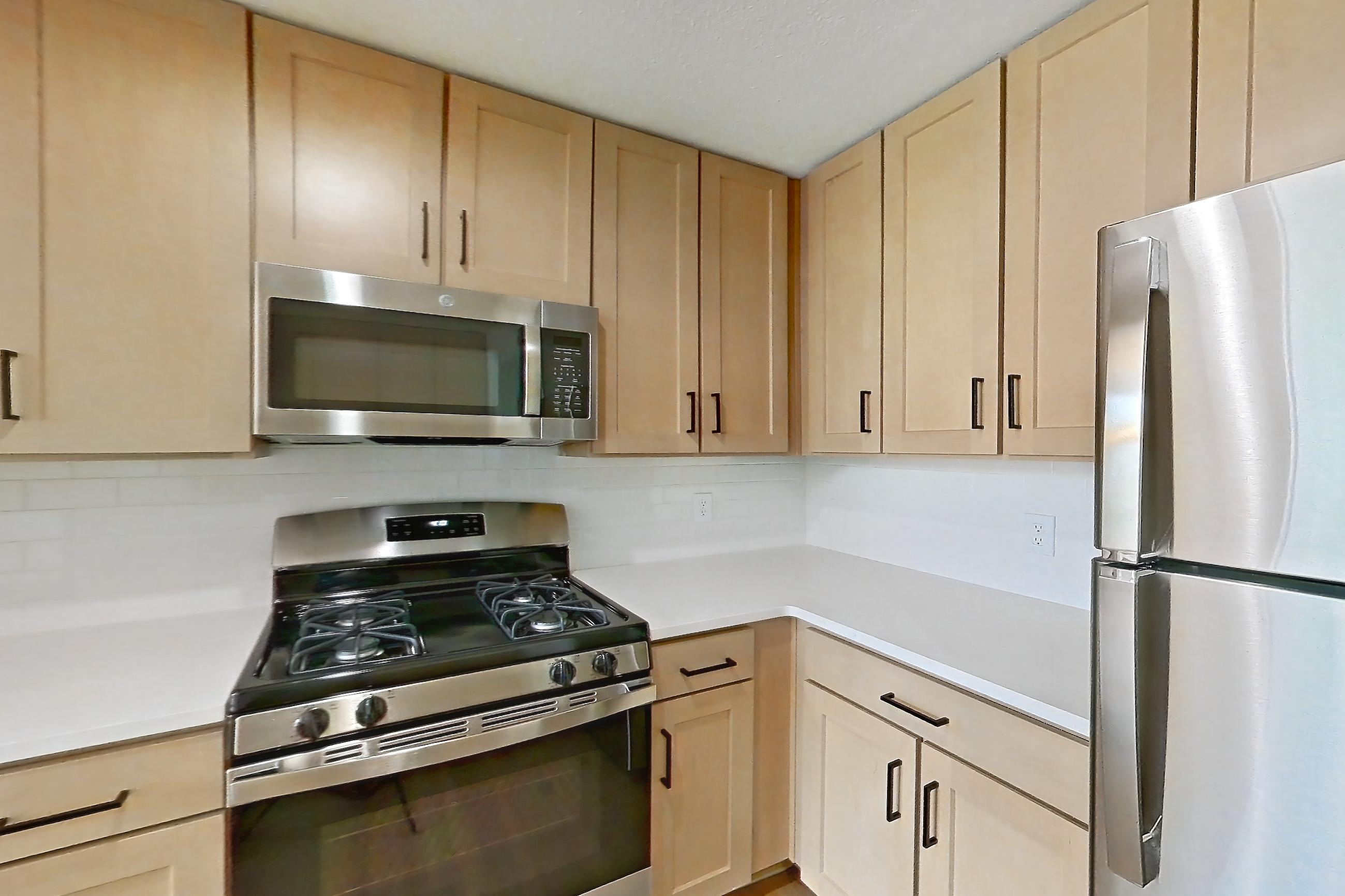 Kitchen with dishwasher, gas range, light countertops, light stone countertops, light wood-finish flooring, microwave, oven/range, and stainless steel appliances, Apartment 2411 at Marquis at Caprock Canyon