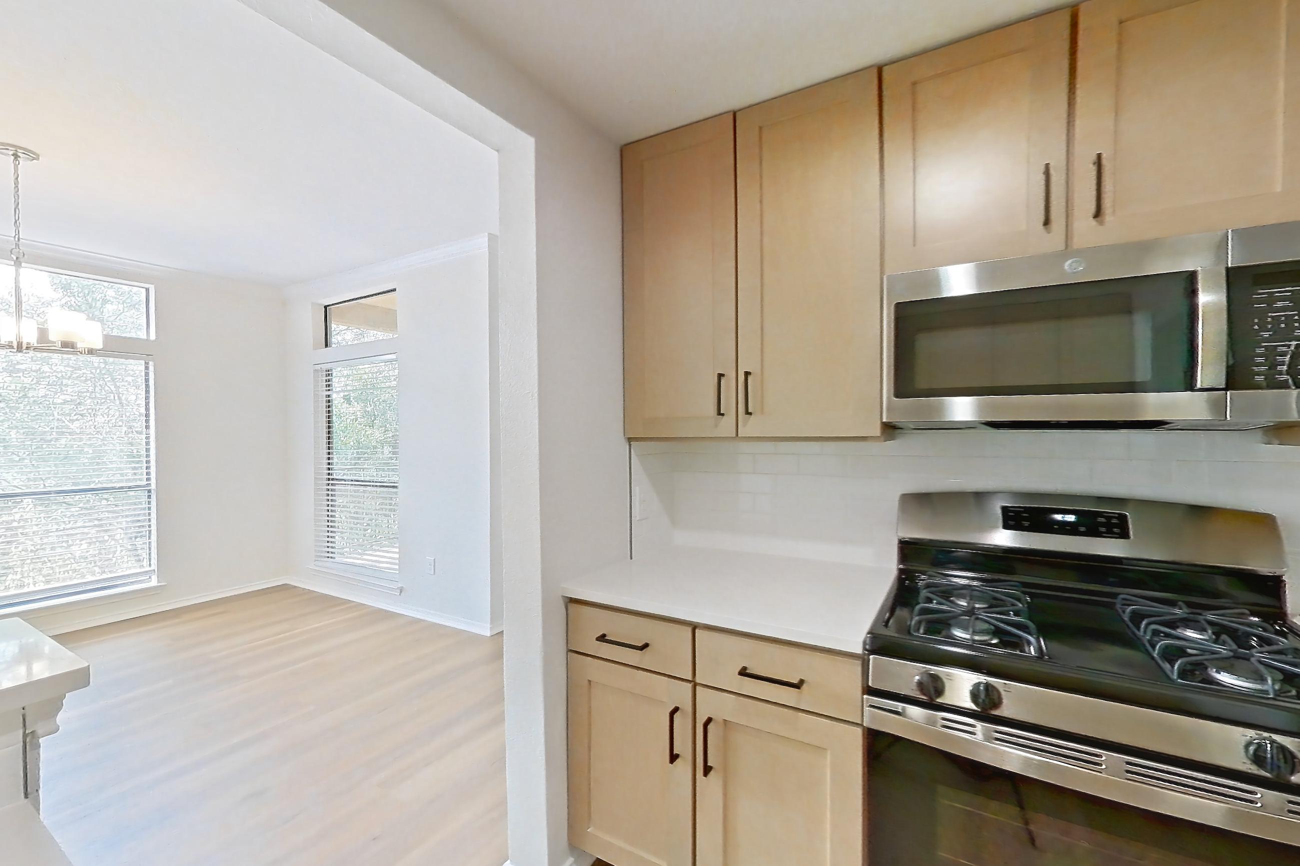 Kitchen with dishwasher, gas range, light countertops, light stone countertops, light wood-finish flooring, microwave, oven/range, and stainless steel appliances, Apartment 2411 at Marquis at Caprock Canyon