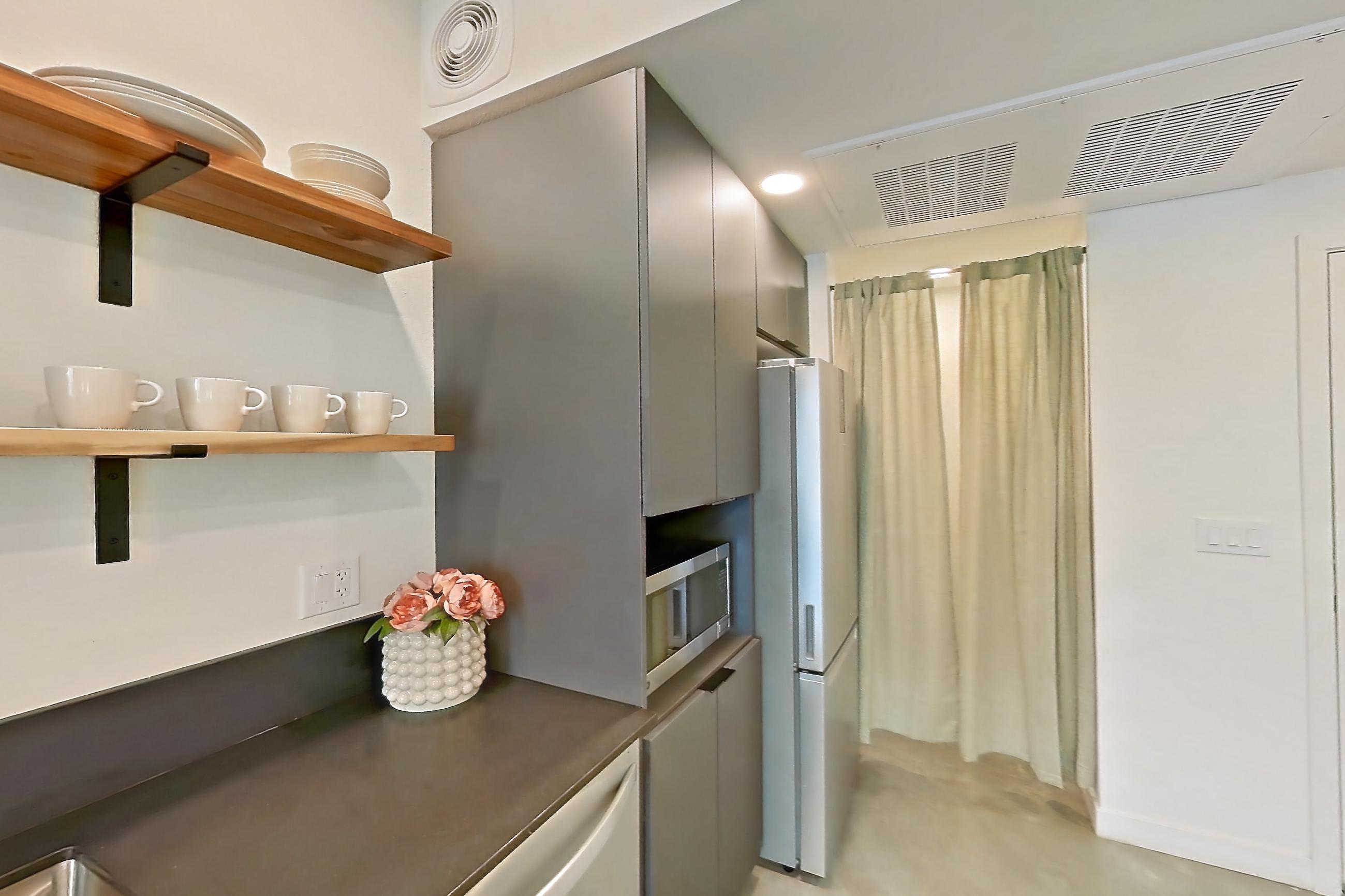 Kitchen with dark countertops, dishwasher, light concrete flooring, microwave, oven/range, polished concrete flooring, refrigerator, stainless steel appliances, and white appliances, Apartment 2002 at Dwell @ 5th and Farmer